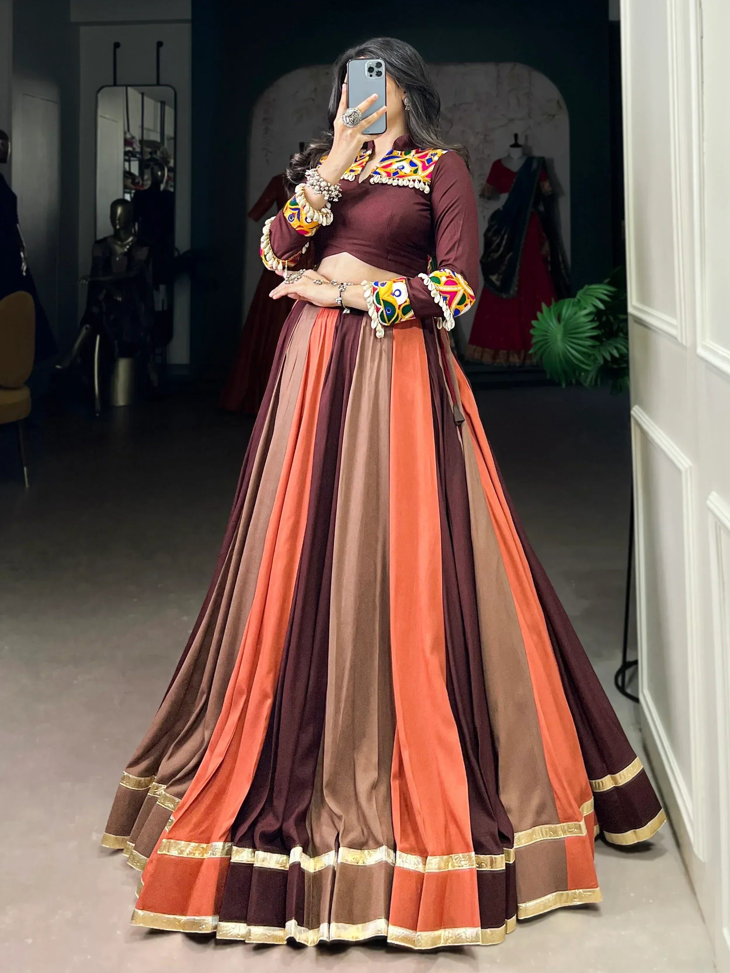 Woman in maroon and orange embroidered lehenga choli with mirror work, perfect for Indian ethnic wear occasions.