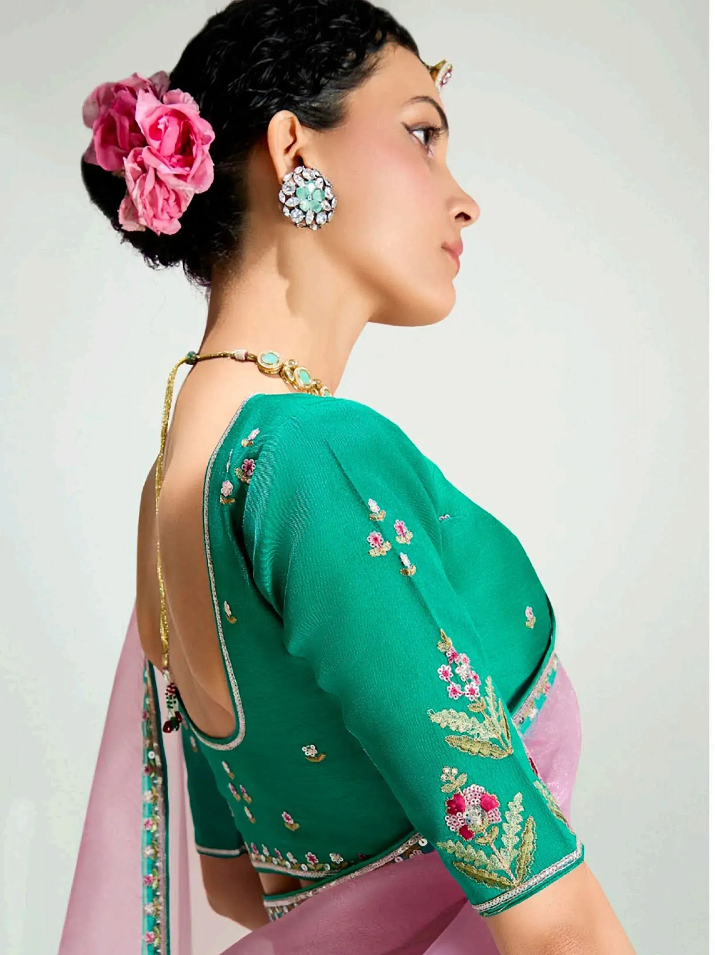 Green embroidered saree blouse with floral details, pink roses in hair, and statement jewelry