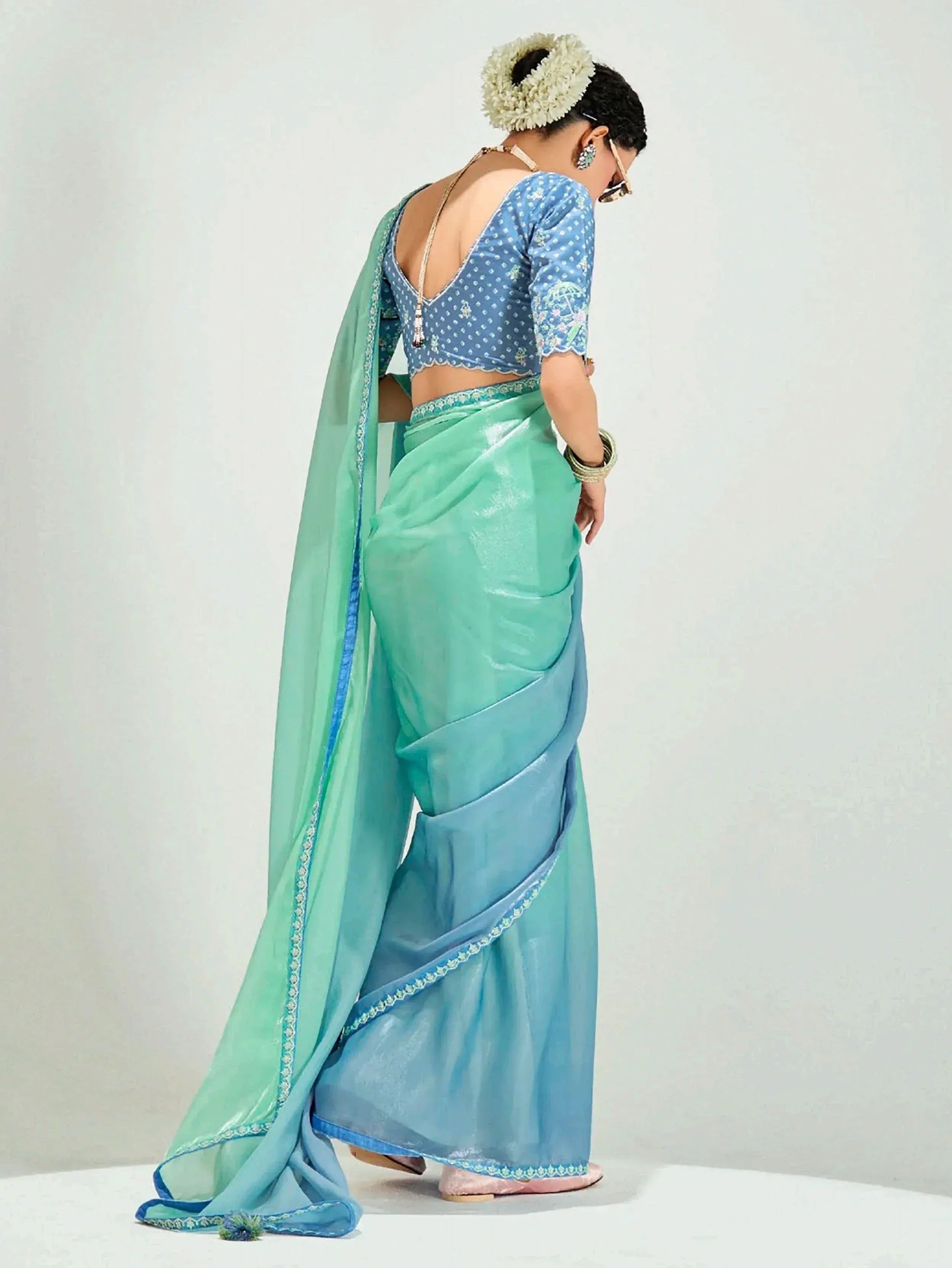 Elegant turquoise saree with blue blouse, floral hair accessory, and intricate embroidery for Indian ethnic wear.