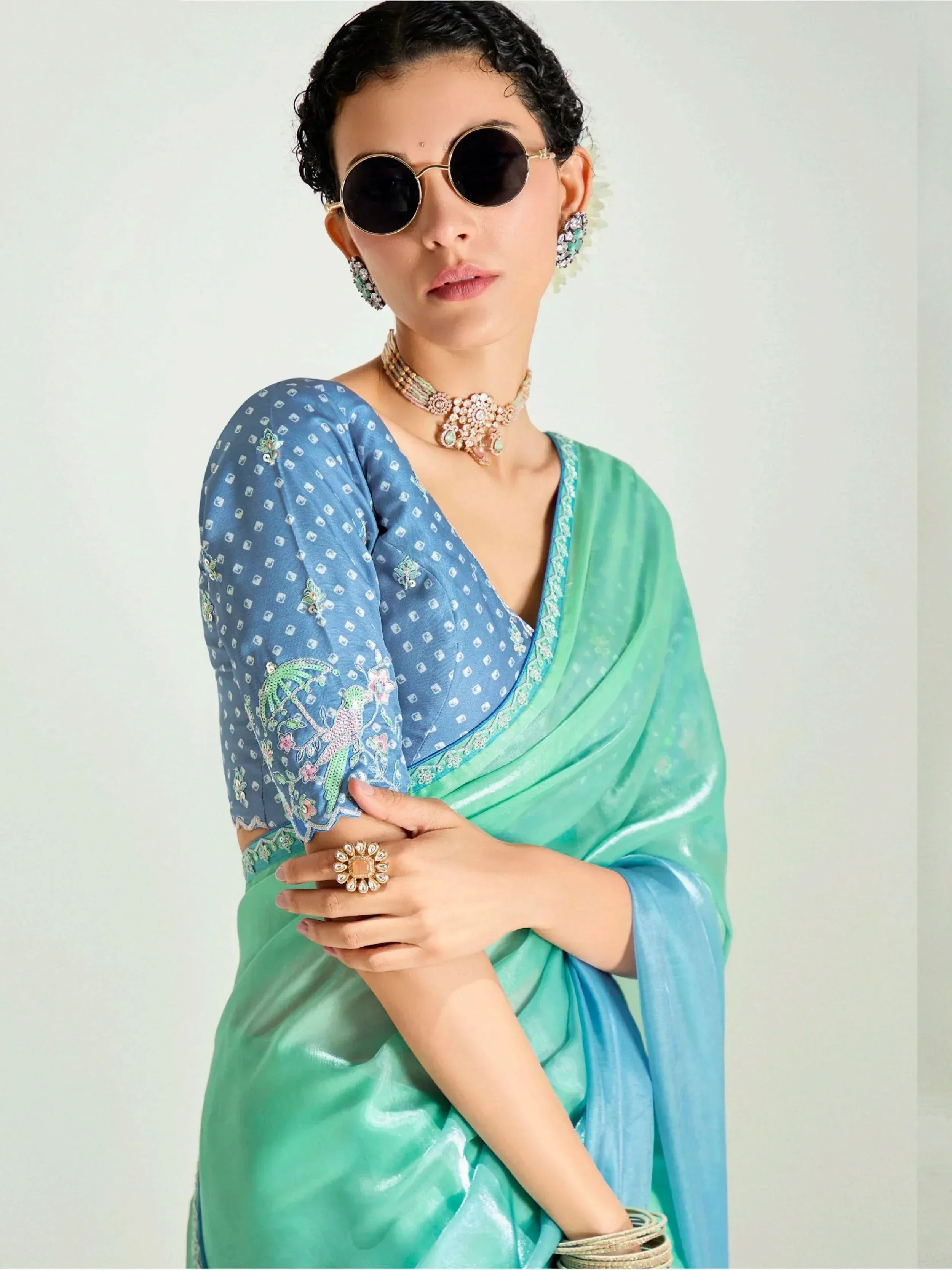 Elegant woman in blue and green embroidered saree with statement jewelry and round sunglasses