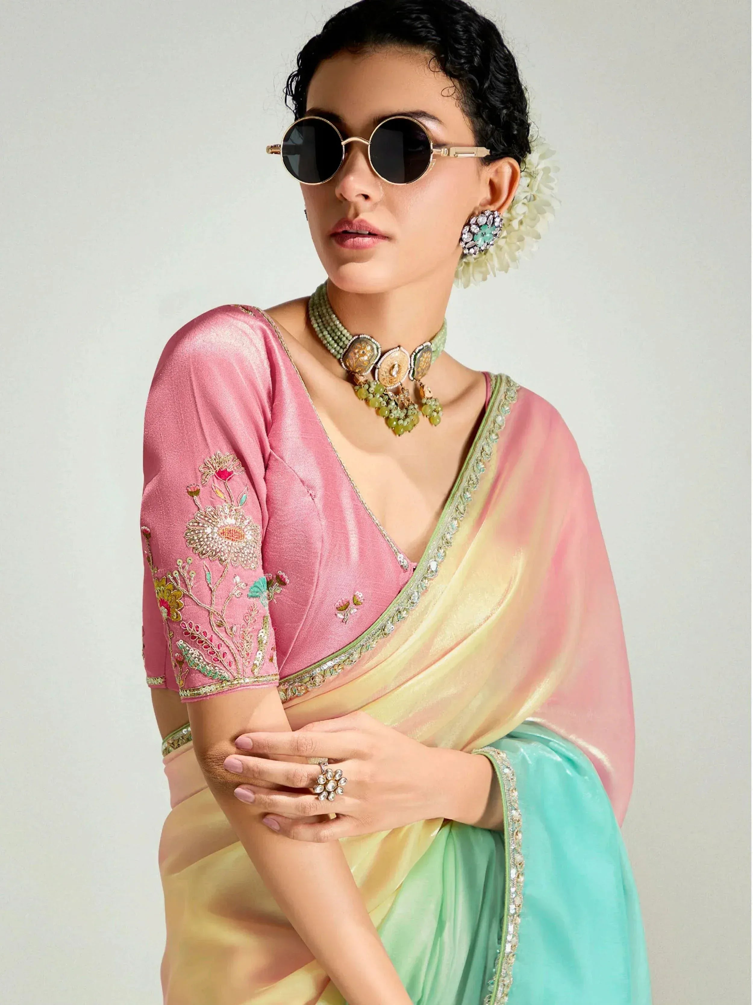 Woman in pink embroidered blouse with pastel ombre saree, floral jewelry, and sunglasses