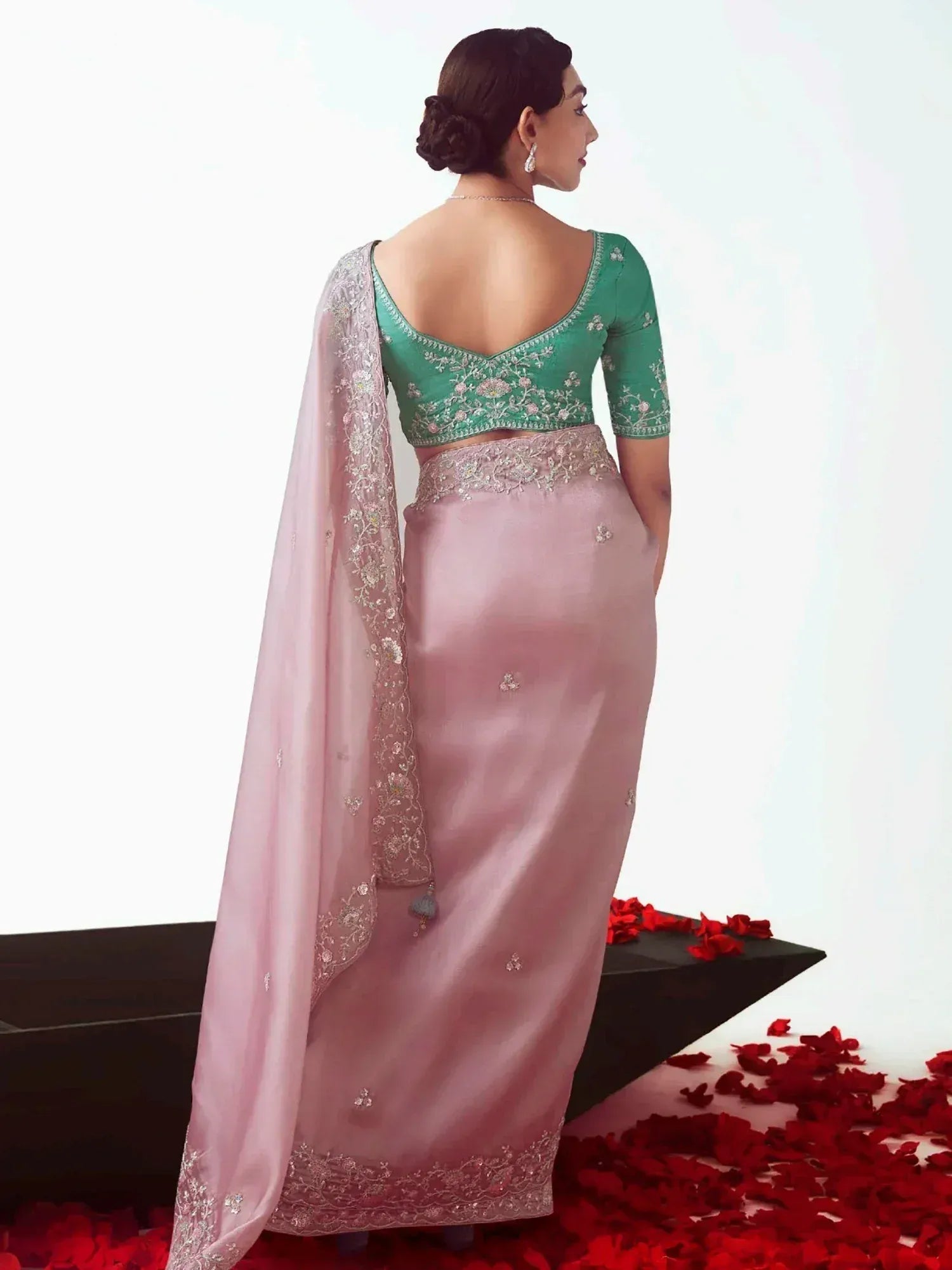 Woman in pink and green embroidered lehenga choli with sheer dupatta, red rose petals on floor