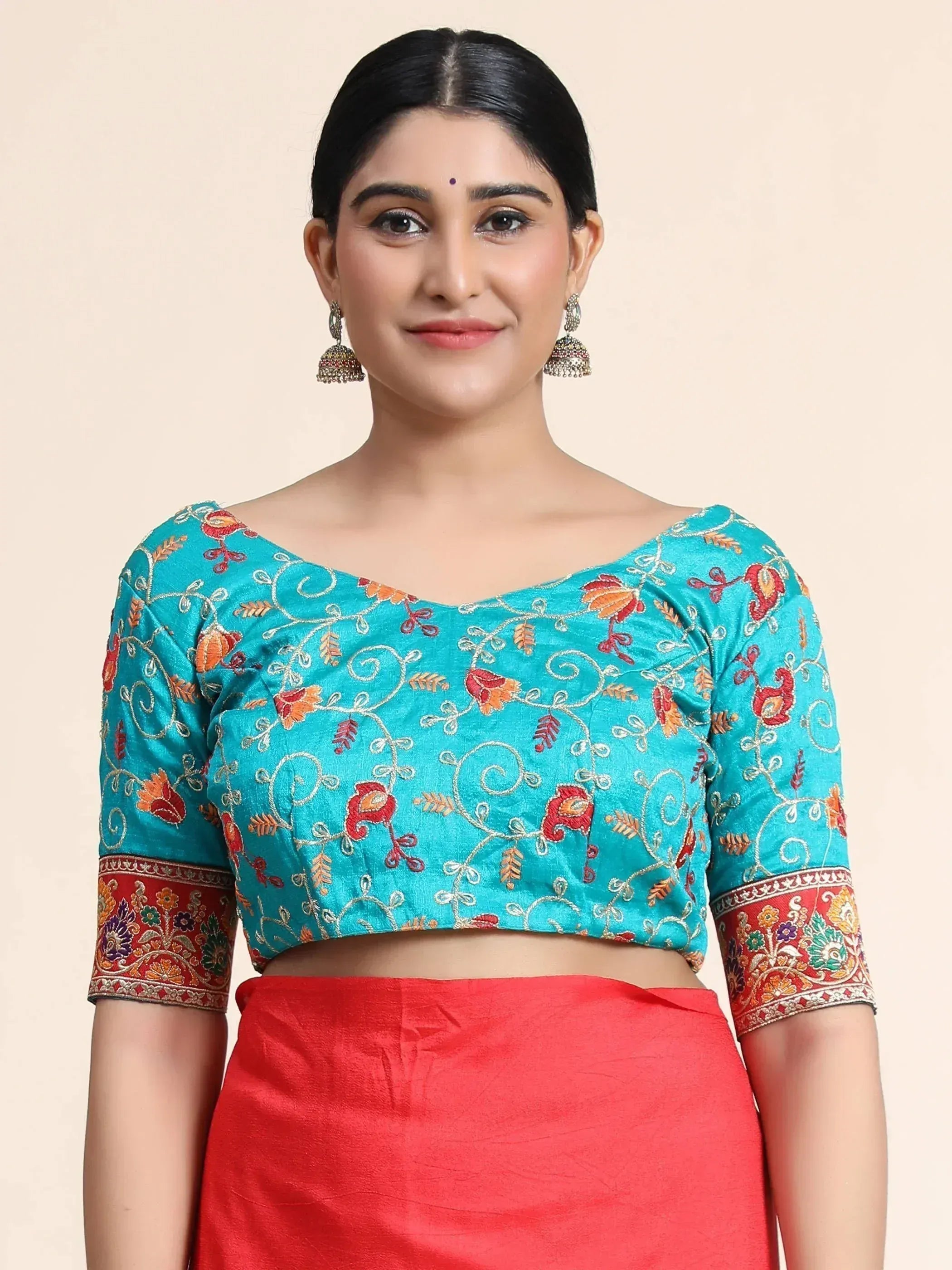 Turquoise embroidered crop top with red floral motifs and contrasting red skirt, styled with jhumka earrings for Indian ethnic wear.