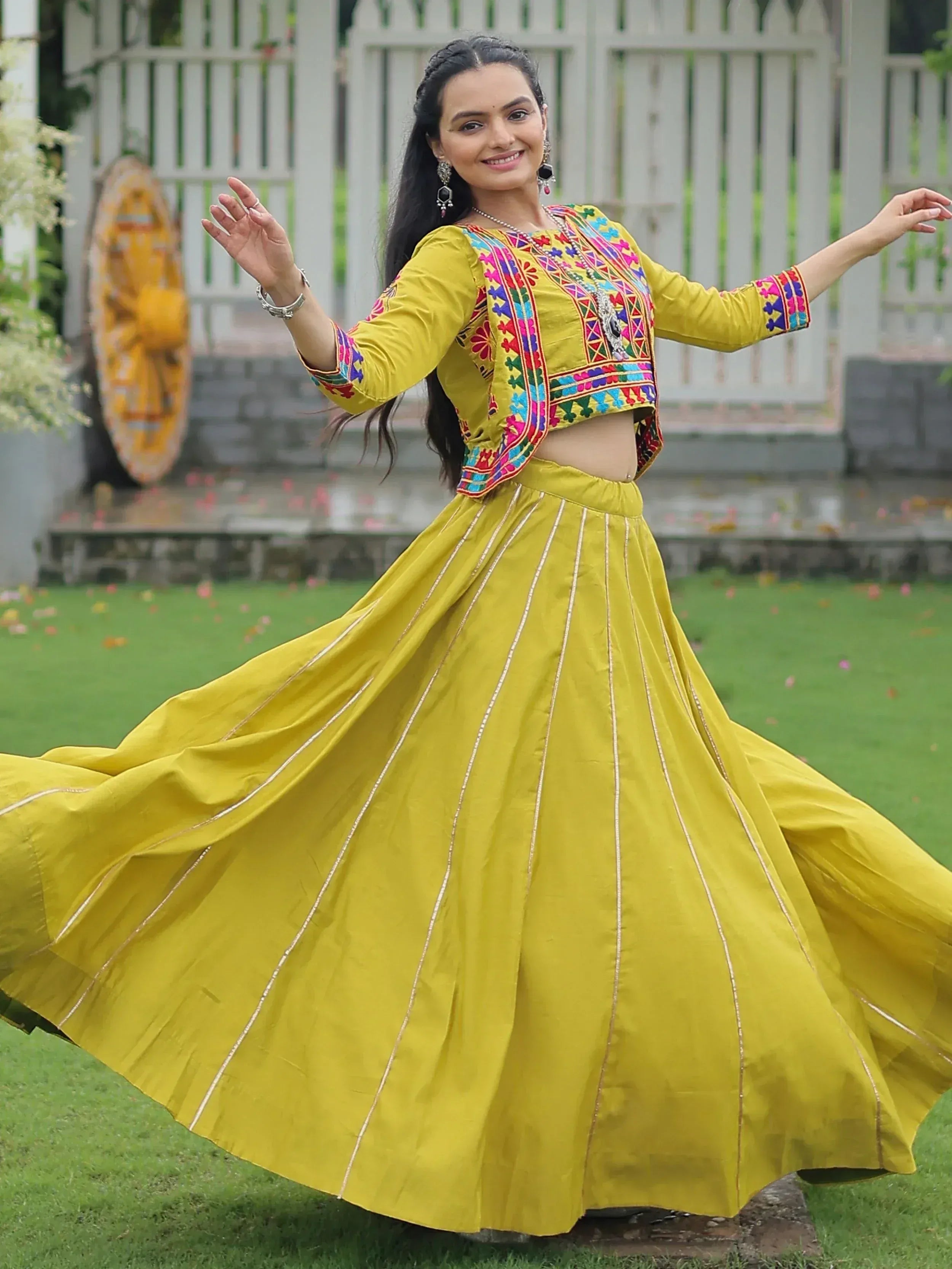 Woman in vibrant yellow ethnic lehenga choli with colorful embroidery, twirling outdoors