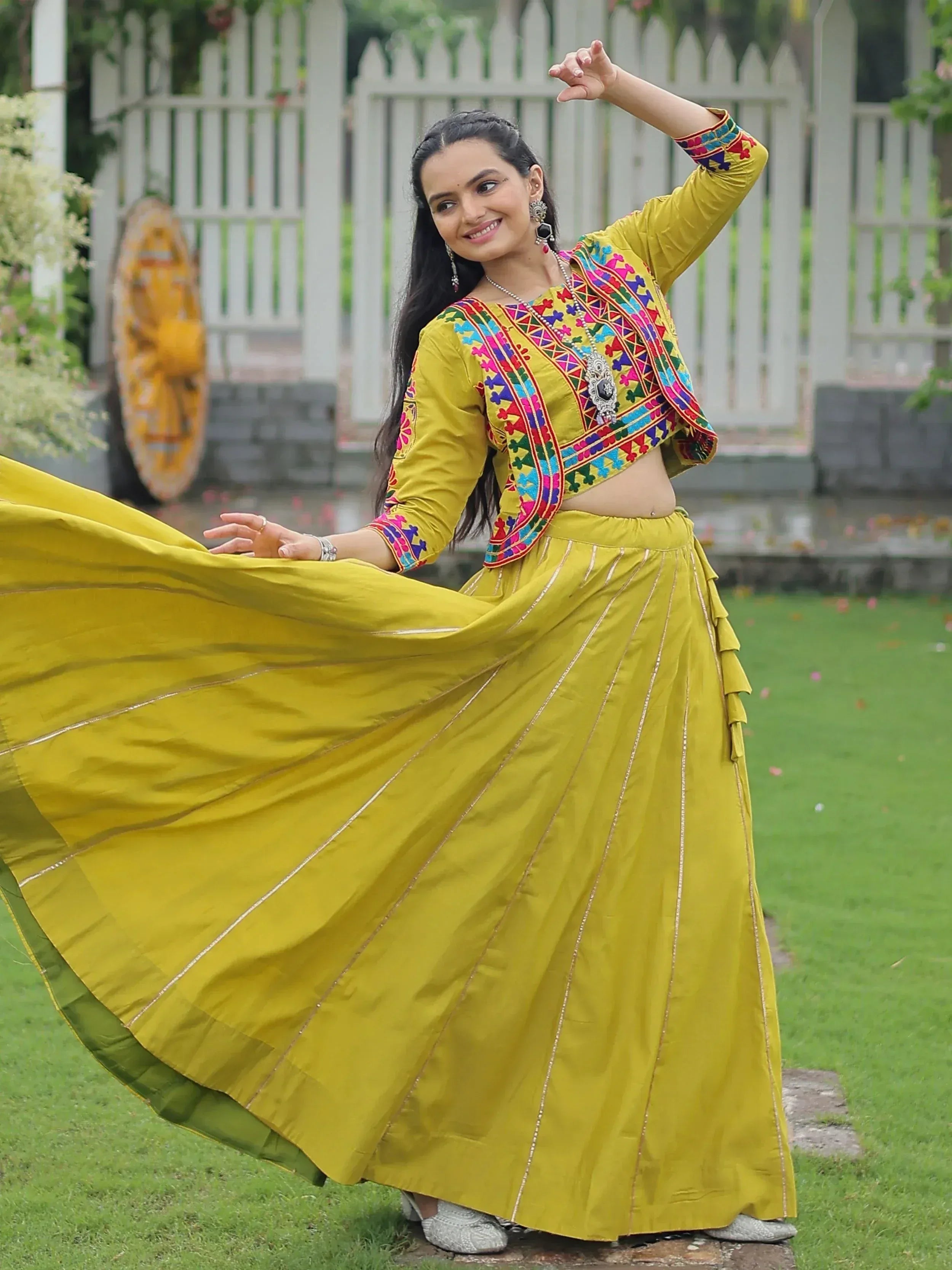 Woman in vibrant yellow ethnic wear with colorful embroidery, twirling in garden