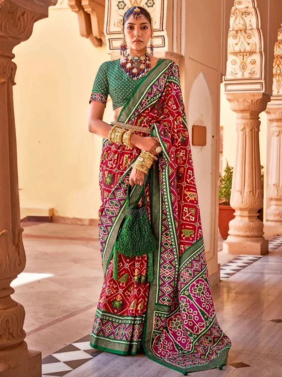 Woman in vibrant red and green printed saree with ethnic jewelry, traditional Indian attire