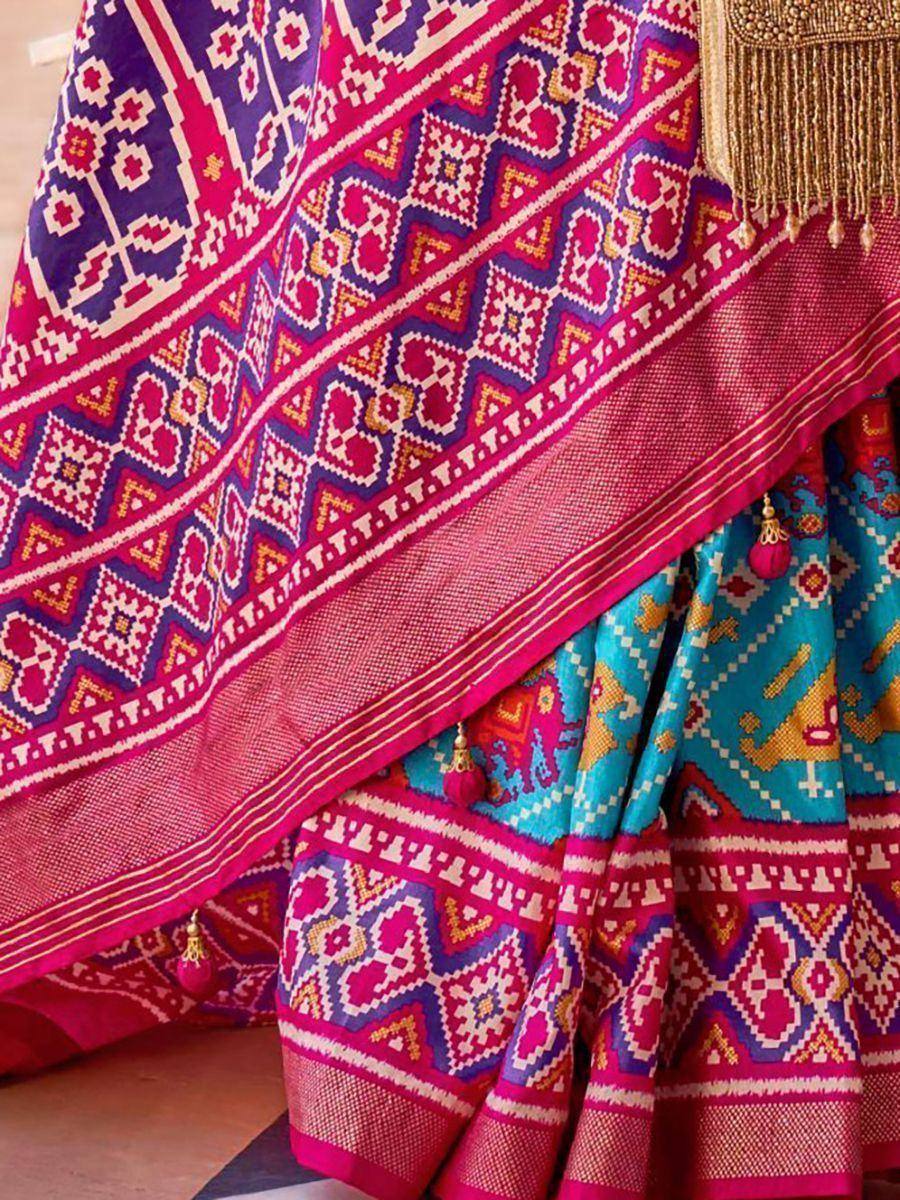 Vibrant pink and blue ethnic lehenga with geometric patterns and gold tassels, perfect for Indian weddings.