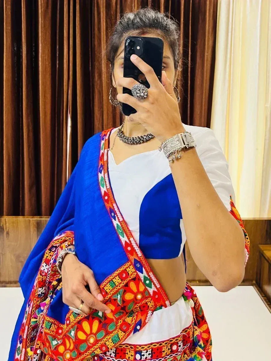 Woman in vibrant blue and red embroidered ethnic saree with mirror work, paired with white blouse and traditional jewelry