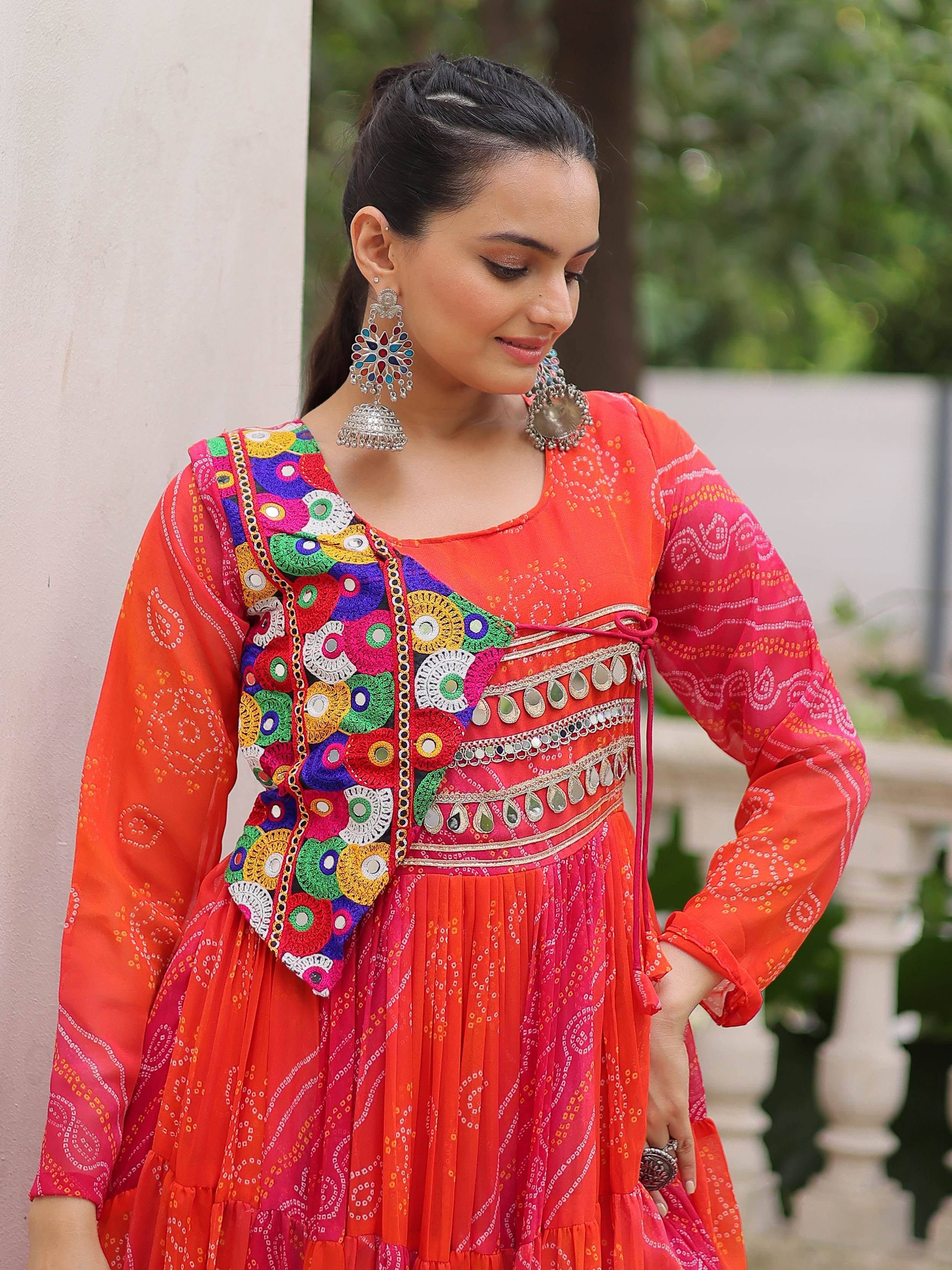 Vibrant orange and pink ethnic gown with mirror work, embroidery, and jhumka earrings for festive occasions