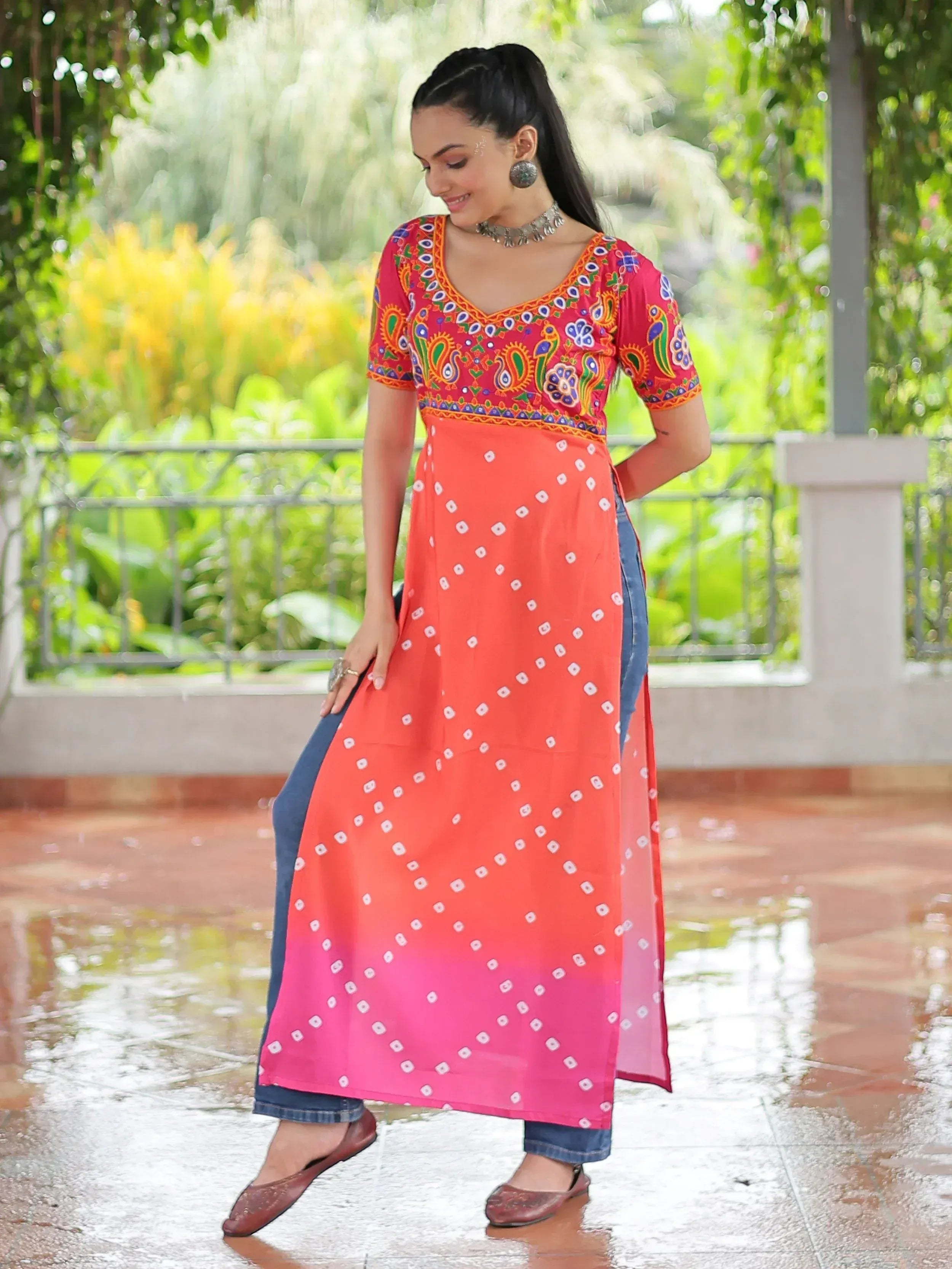 Woman in vibrant Indian ethnic kurti with paisley print, ombre skirt, and denim jeans, styled for casual wear.
