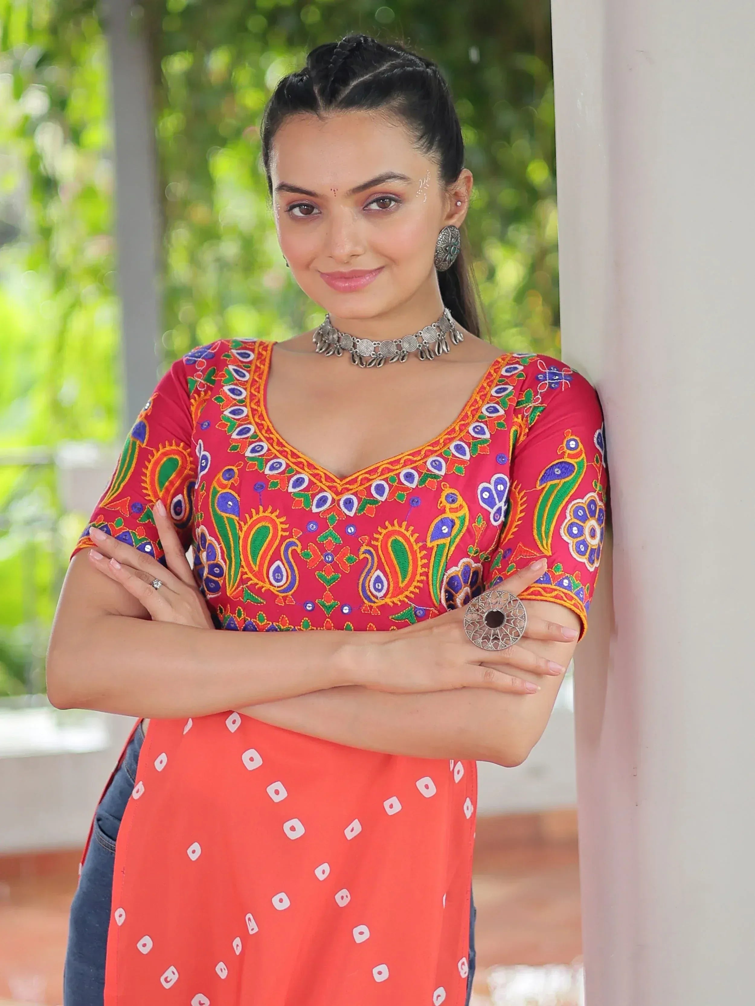 Woman in vibrant red embroidered kurta with peacock motifs, paired with orange printed skirt and silver jewelry