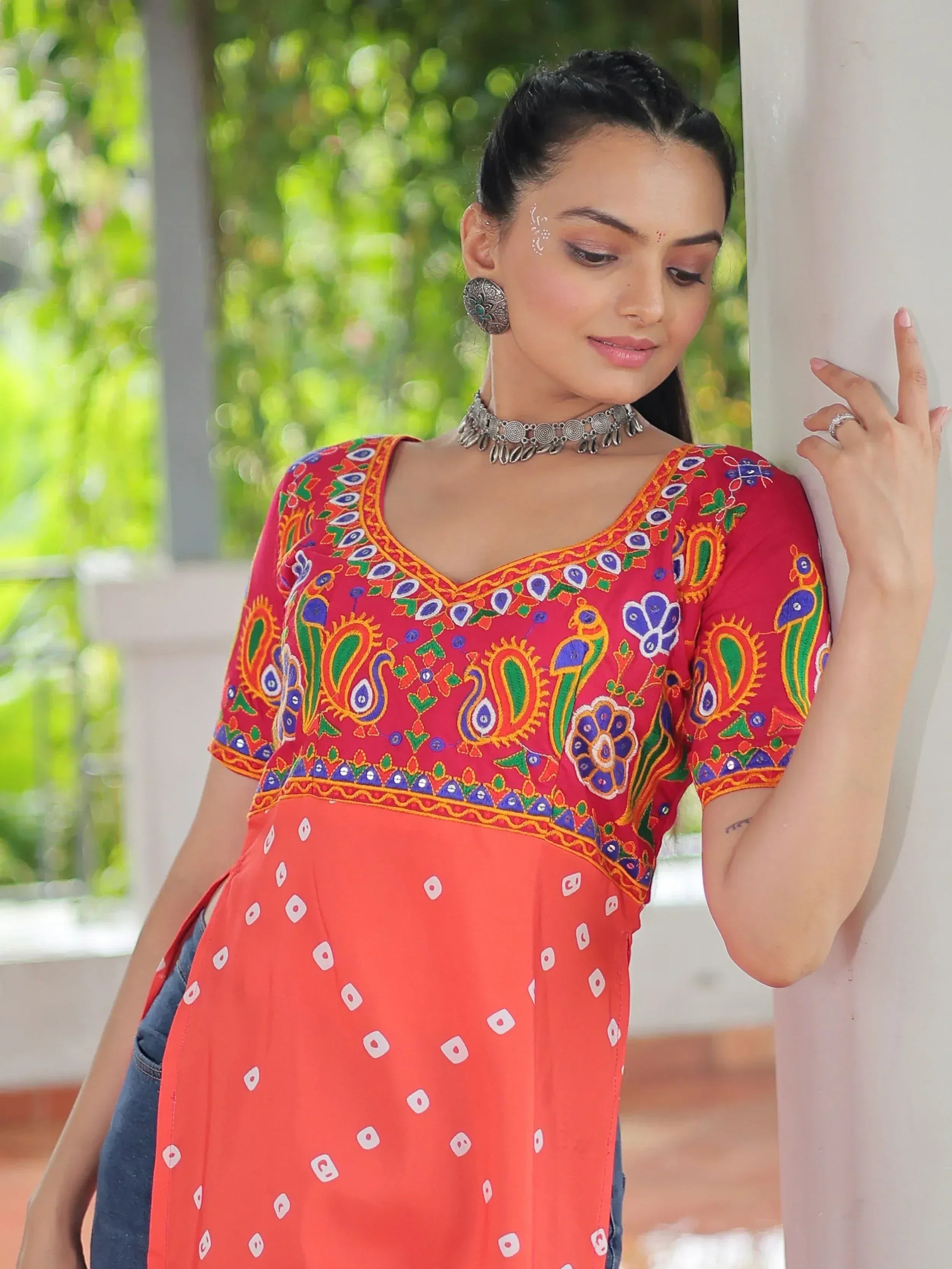 Red and orange embroidered ethnic kurti with peacock motifs, paired with jeans, perfect for casual Indian wear.
