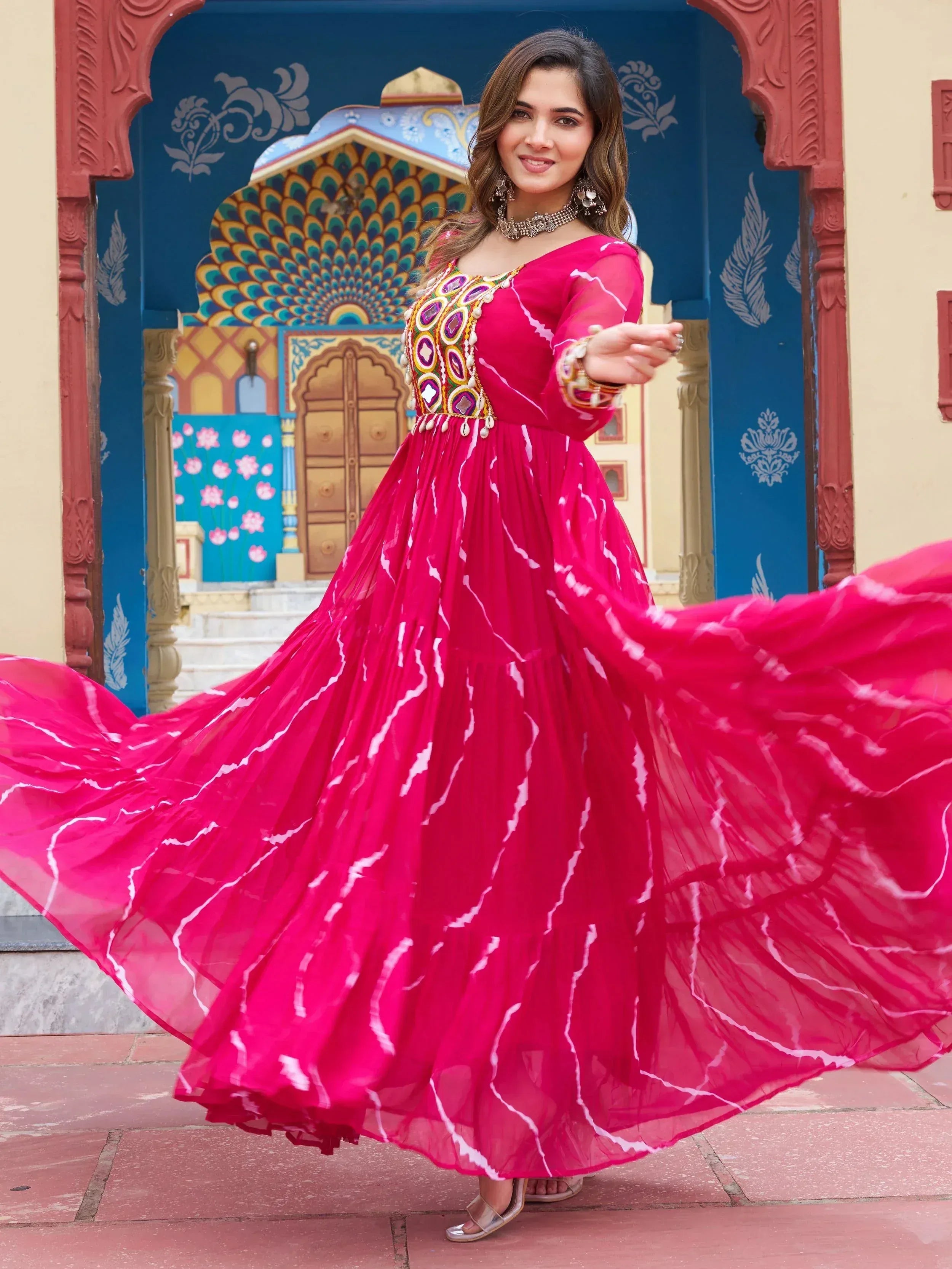 Woman in vibrant pink ethnic gown with mirror work, twirling against colorful Indian architecture
