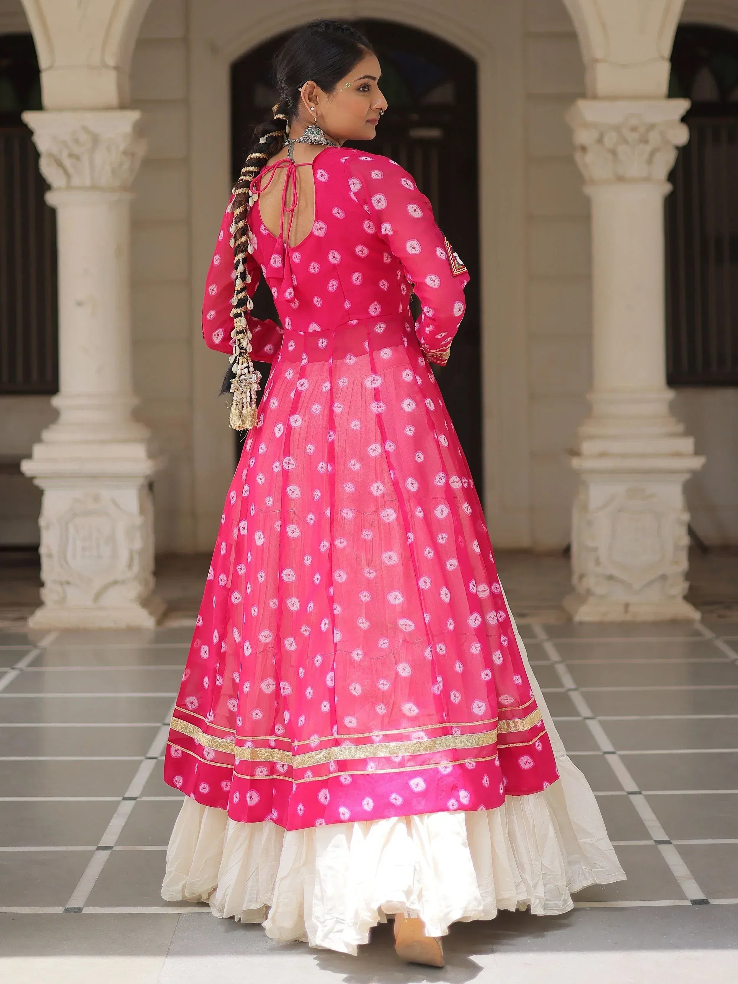 Pink printed anarkali with gold trim, white underskirt, and traditional jewelry, styled for Indian ethnic wear.