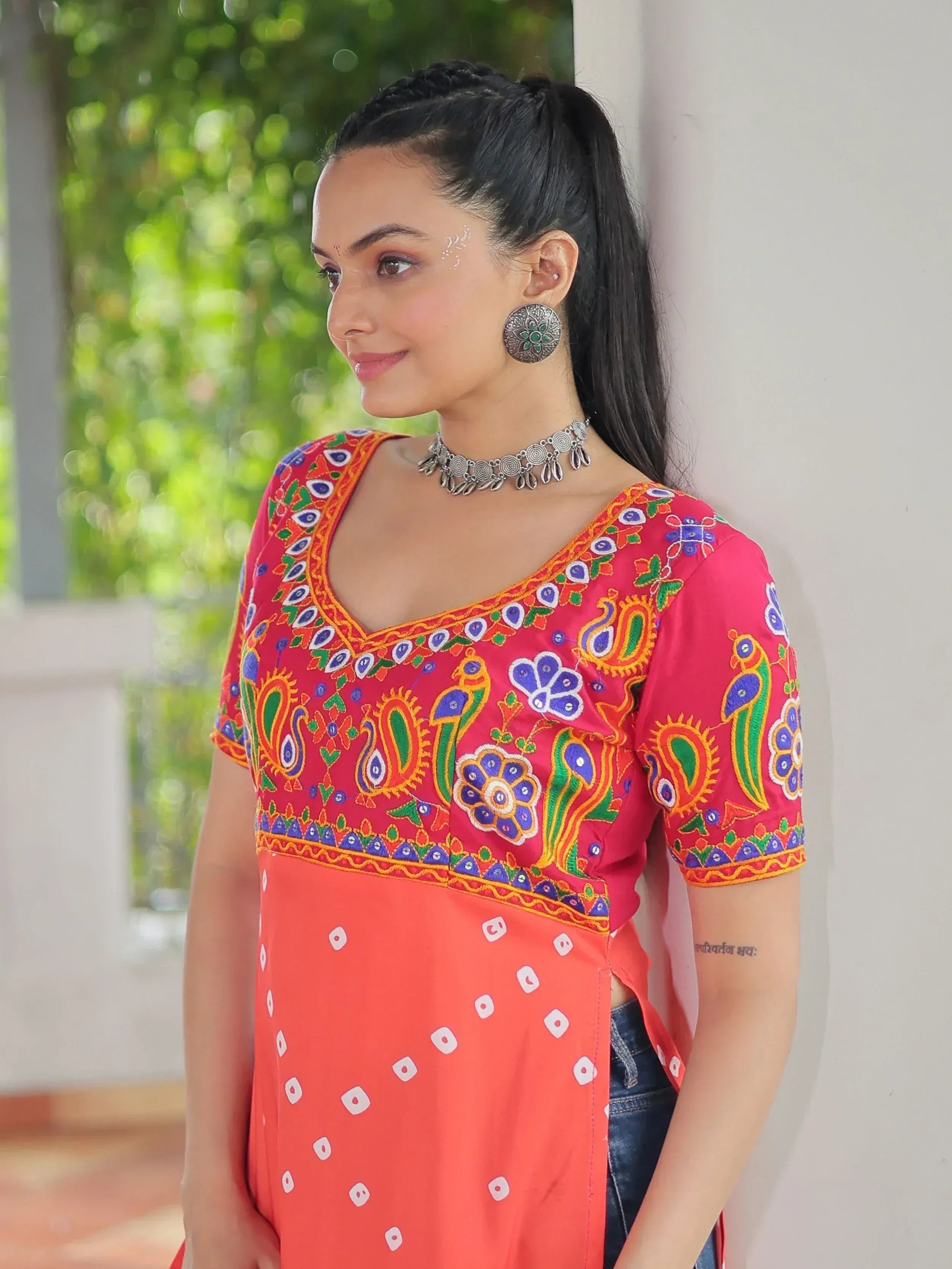 Woman in vibrant pink embroidered kurta with peacock motifs, paired with orange printed skirt and silver jewelry