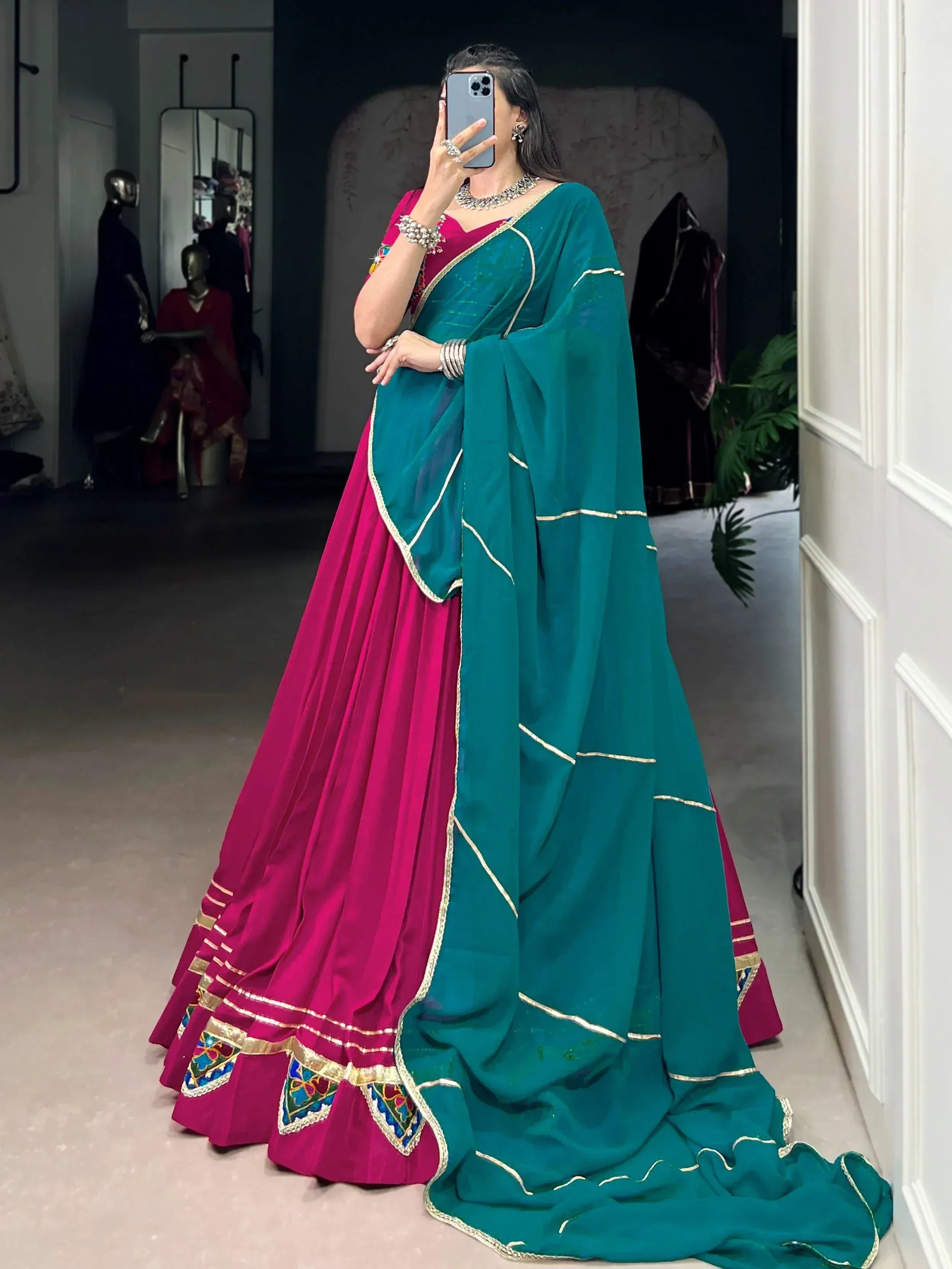 Woman in vibrant pink and teal designer lehenga choli with gold embroidery, perfect for Indian ethnic wear events.