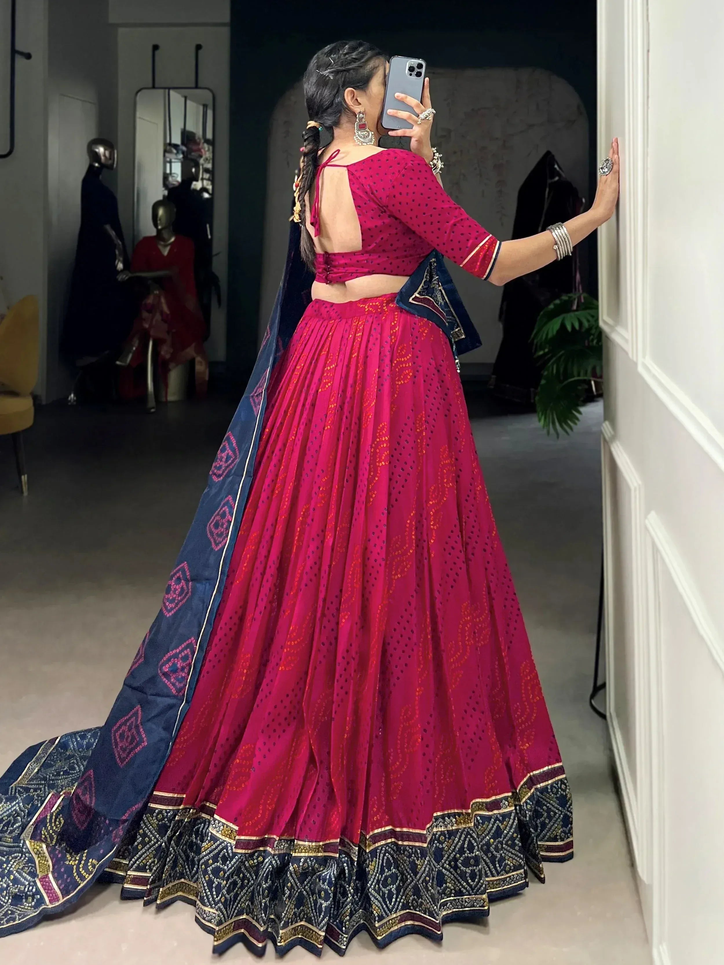 Woman in vibrant pink lehenga choli with blue dupatta, taking mirror selfie in boutique