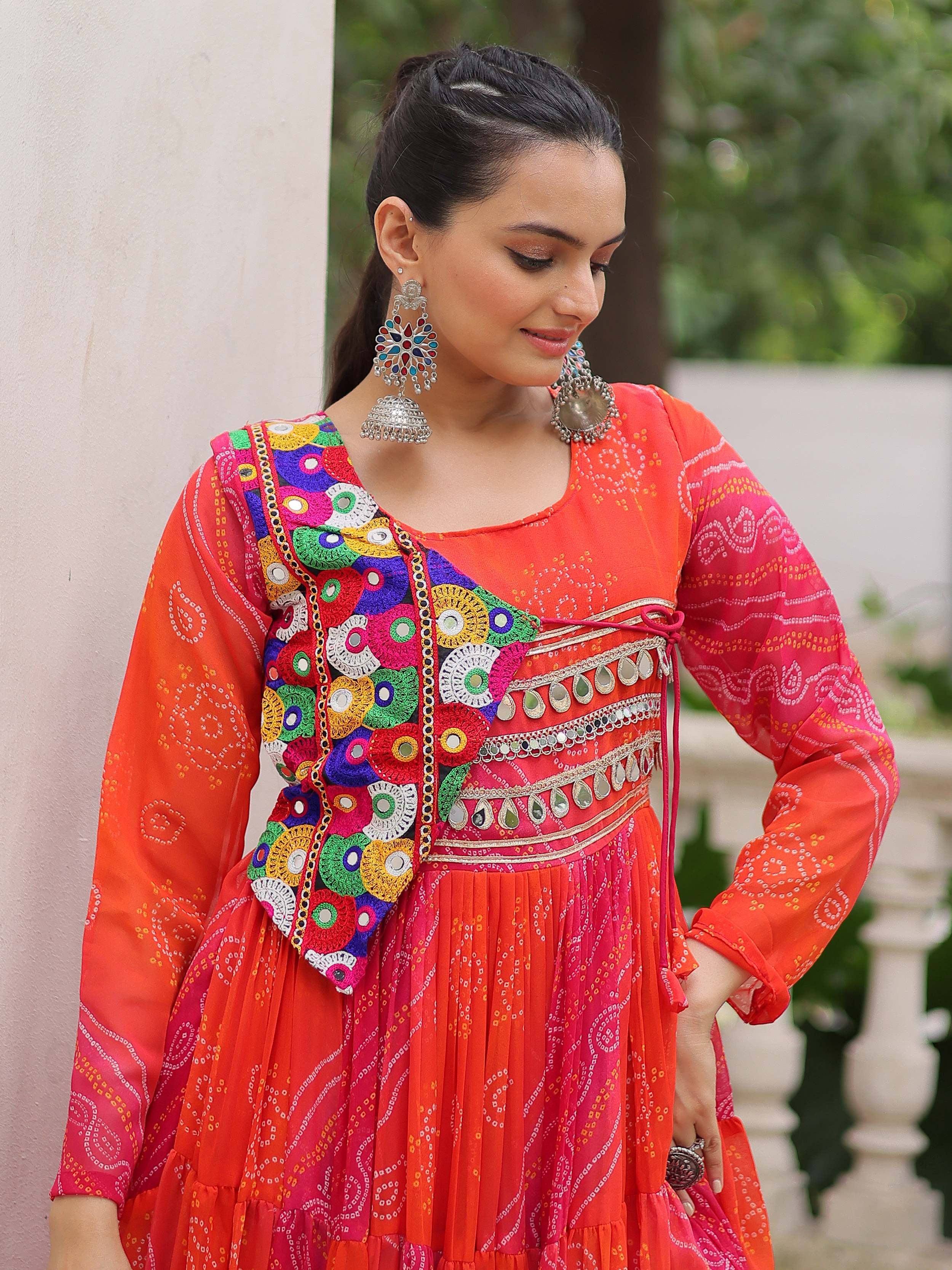 Vibrant orange and pink ethnic gown with mirror work, embroidery, and jhumka earrings for festive occasions