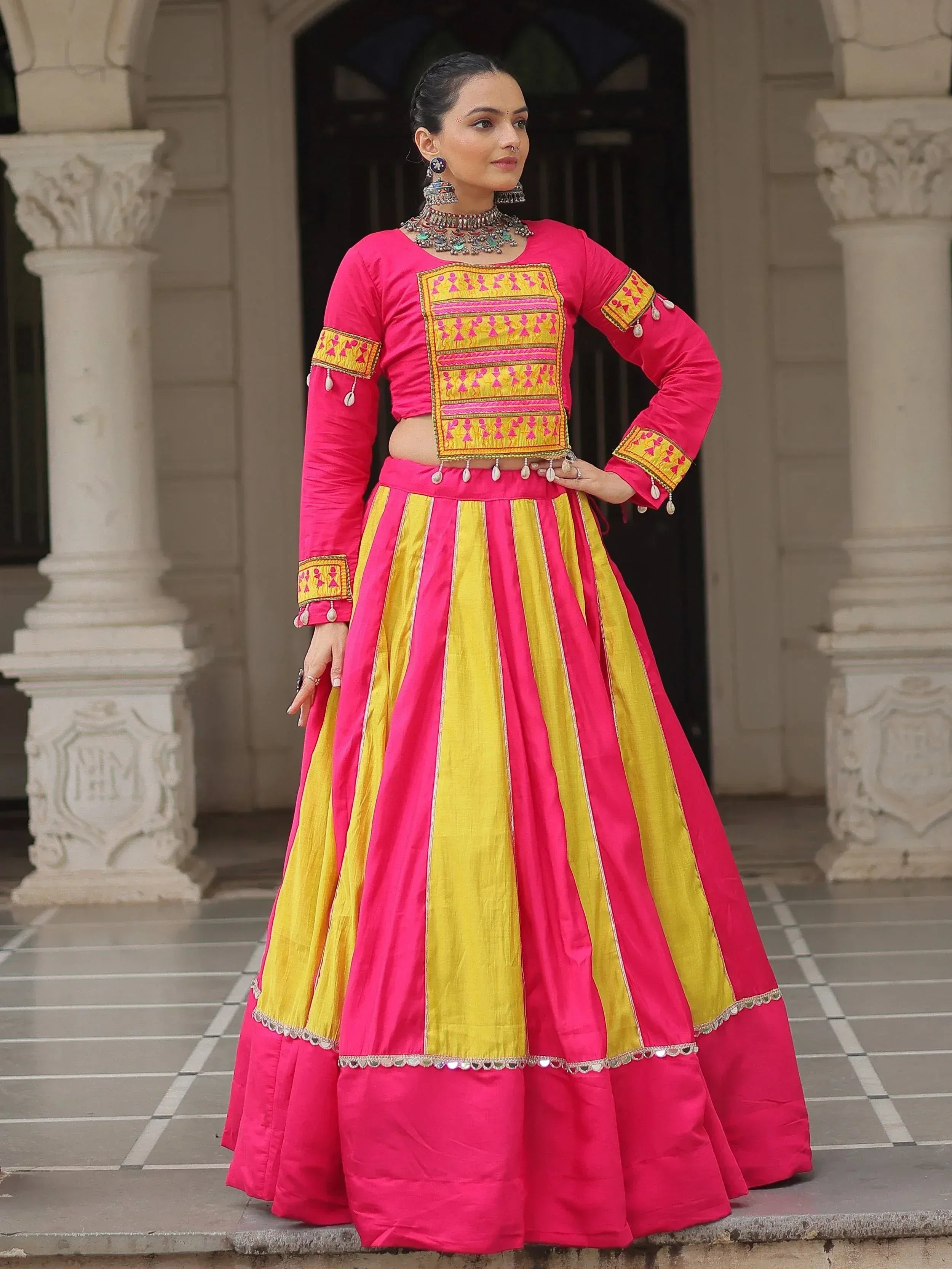 Vibrant pink and yellow ethnic lehenga choli with intricate embroidery and mirror work, perfect for festive occasions.