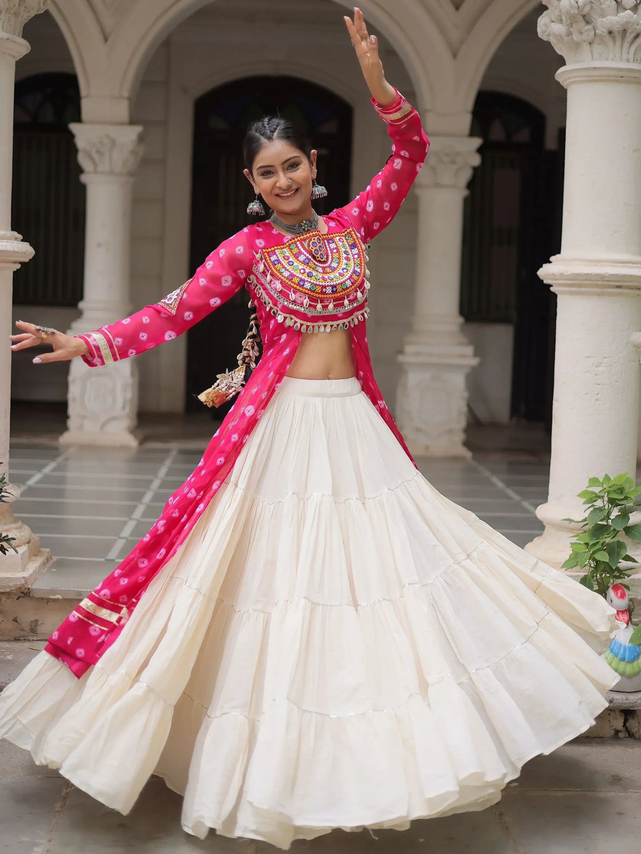 Woman in vibrant pink and white Indian ethnic wear with mirror work, dancing in courtyard