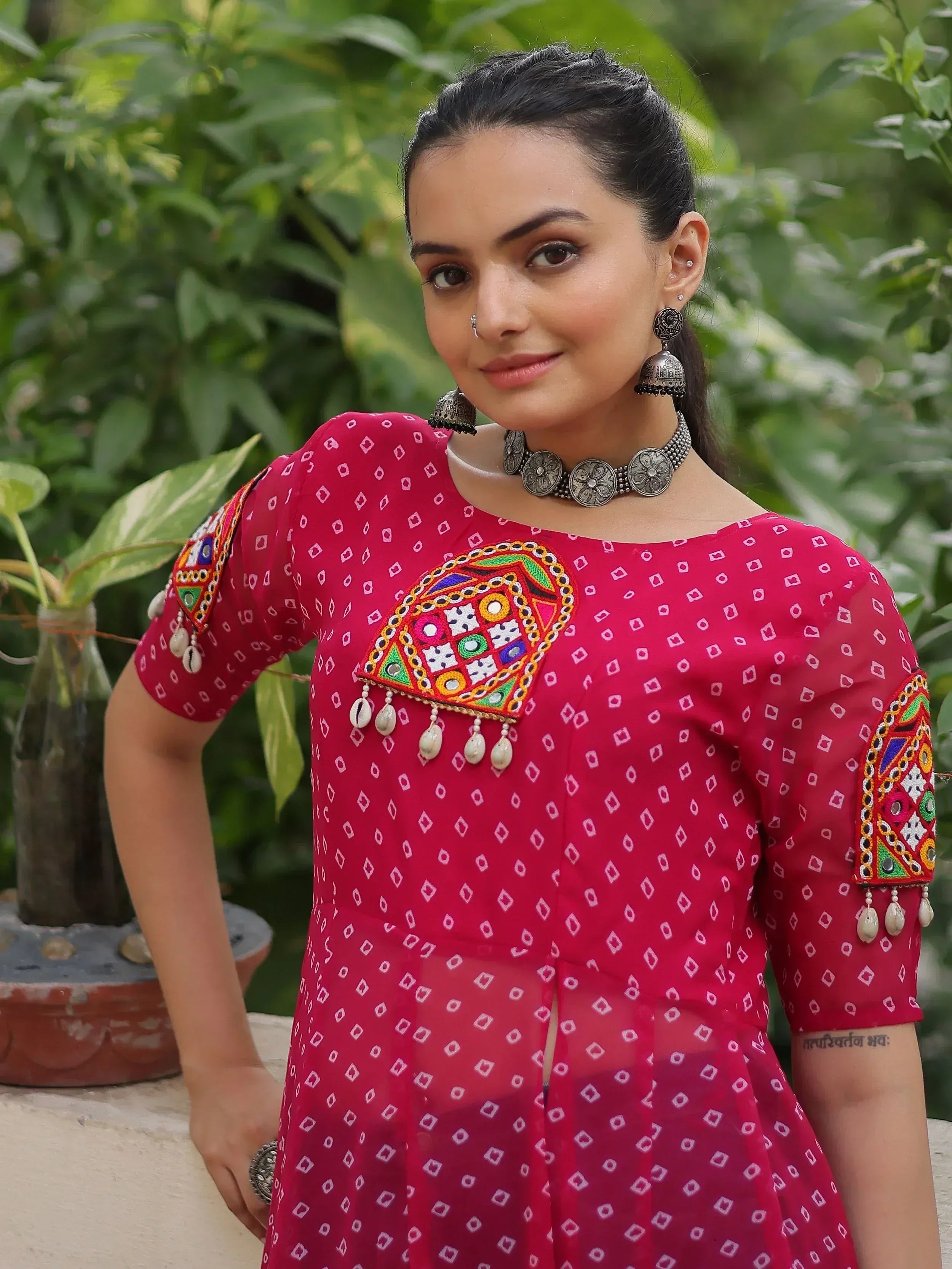 Woman in vibrant red ethnic kurta with mirror work, embroidery, and shell tassels, paired with silver jewelry.