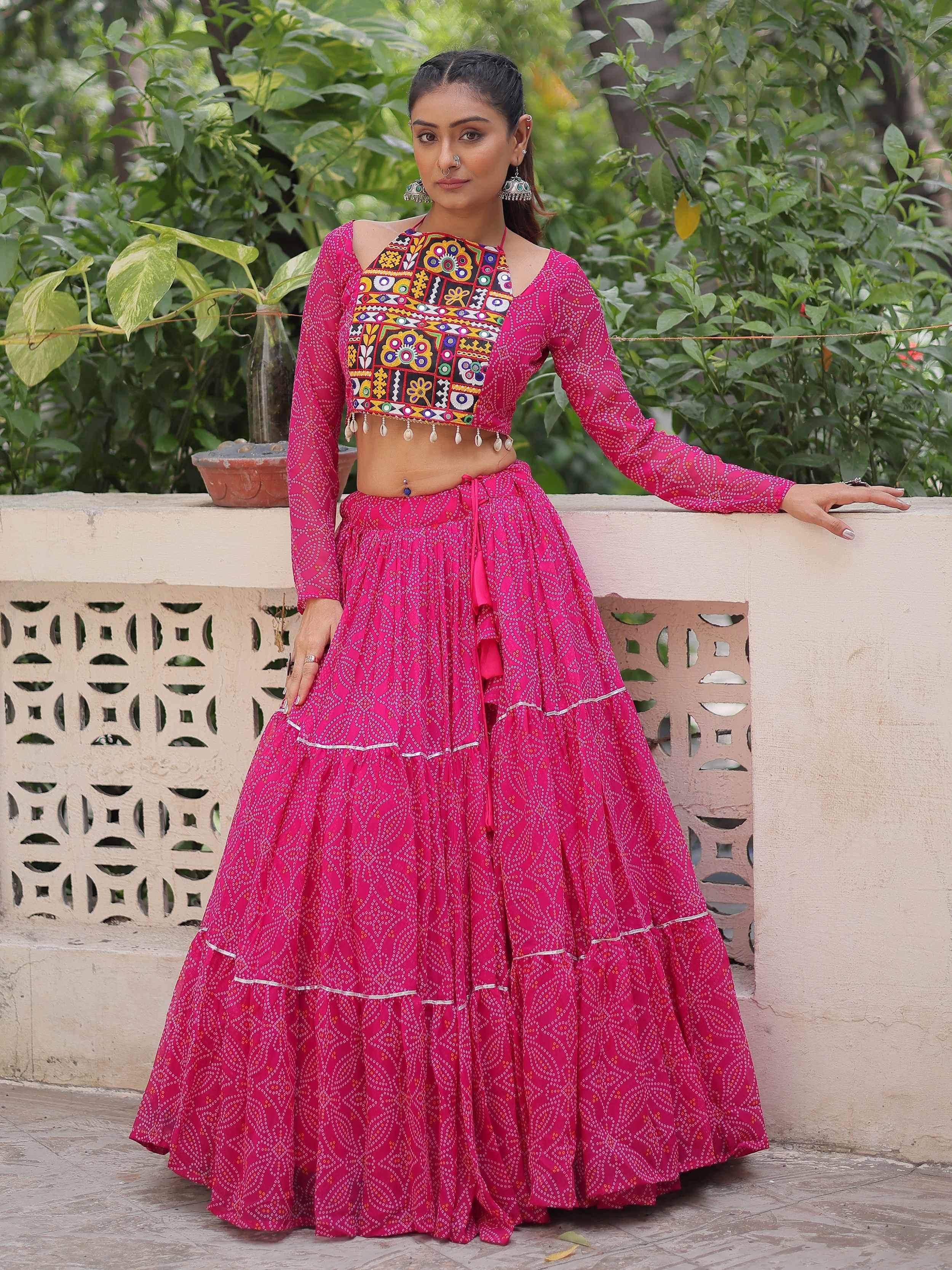 Vibrant pink ethnic lehenga choli with mirror work blouse and tiered skirt, perfect for Indian festive occasions.