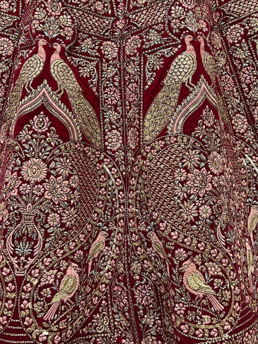 Rich maroon velvet lehenga with intricate gold and pink peacock embroidery, perfect for Indian ethnic wear.