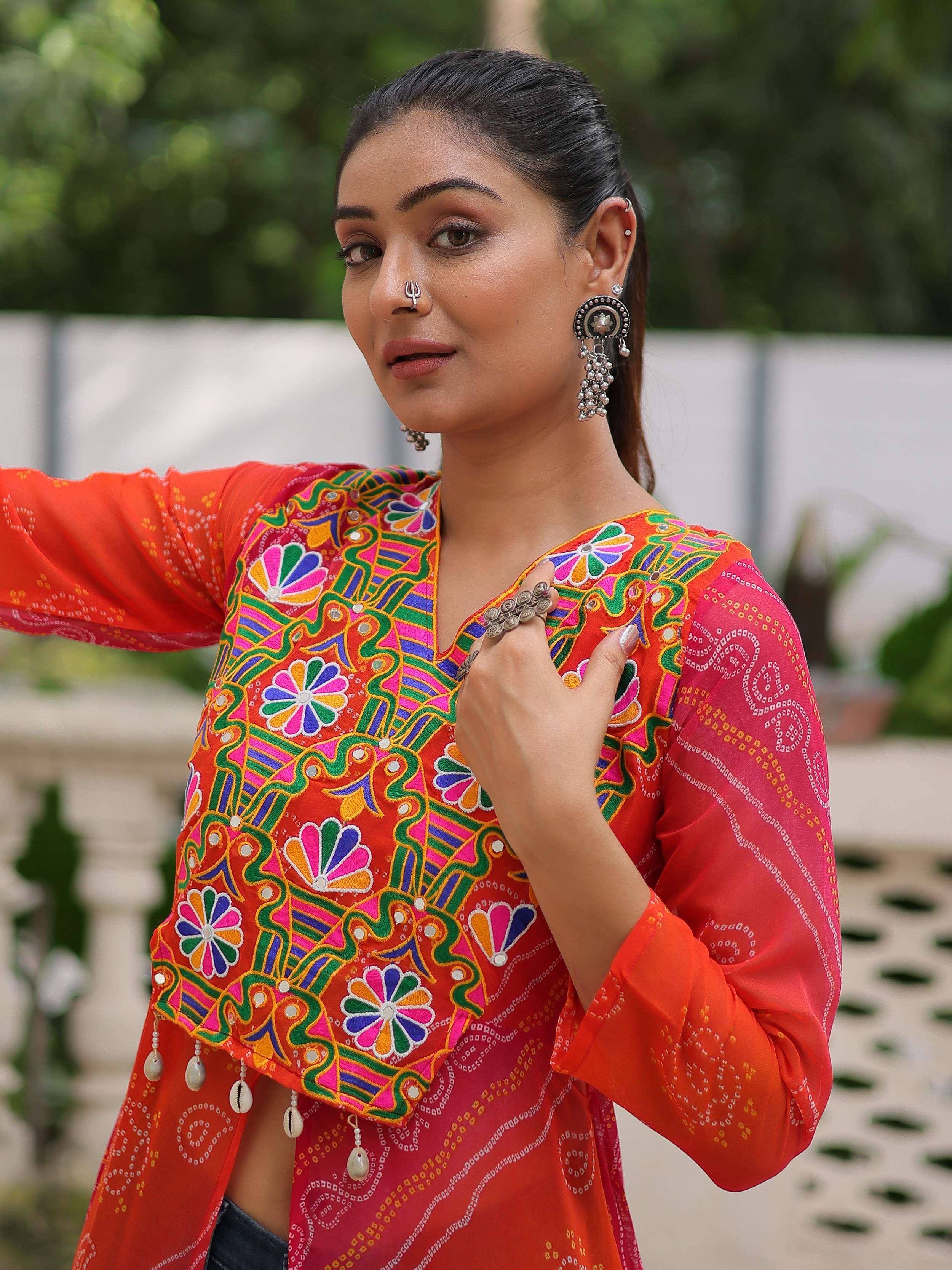 Vibrant orange ethnic kurti with colorful floral embroidery and mirror work, paired with traditional jewelry.