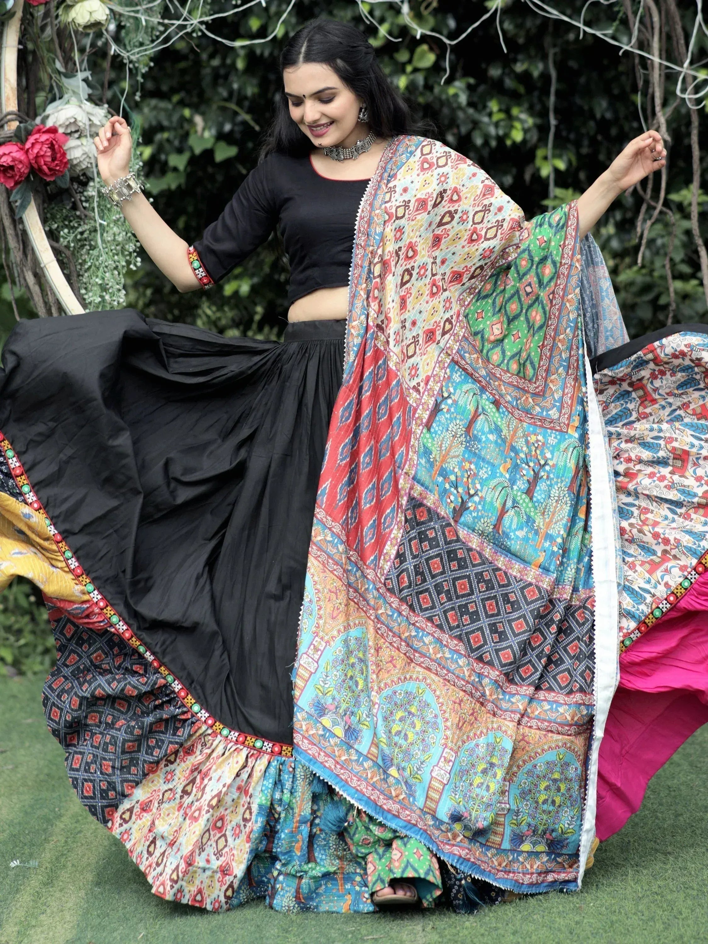 Woman in black lehenga choli with colorful printed dupatta, dancing outdoors