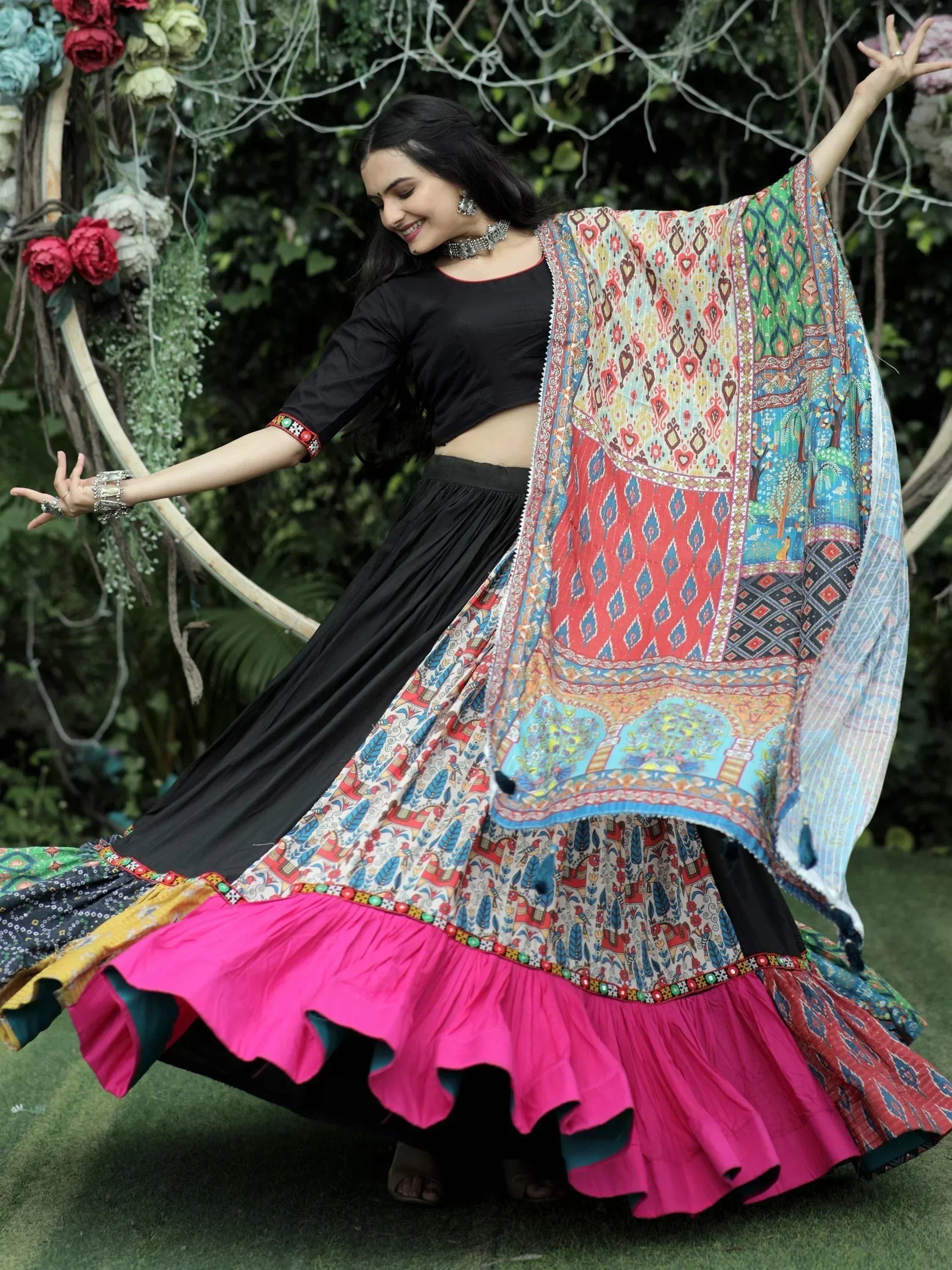 Woman in black crop top and colorful printed lehenga with pink ruffle, twirling outdoors