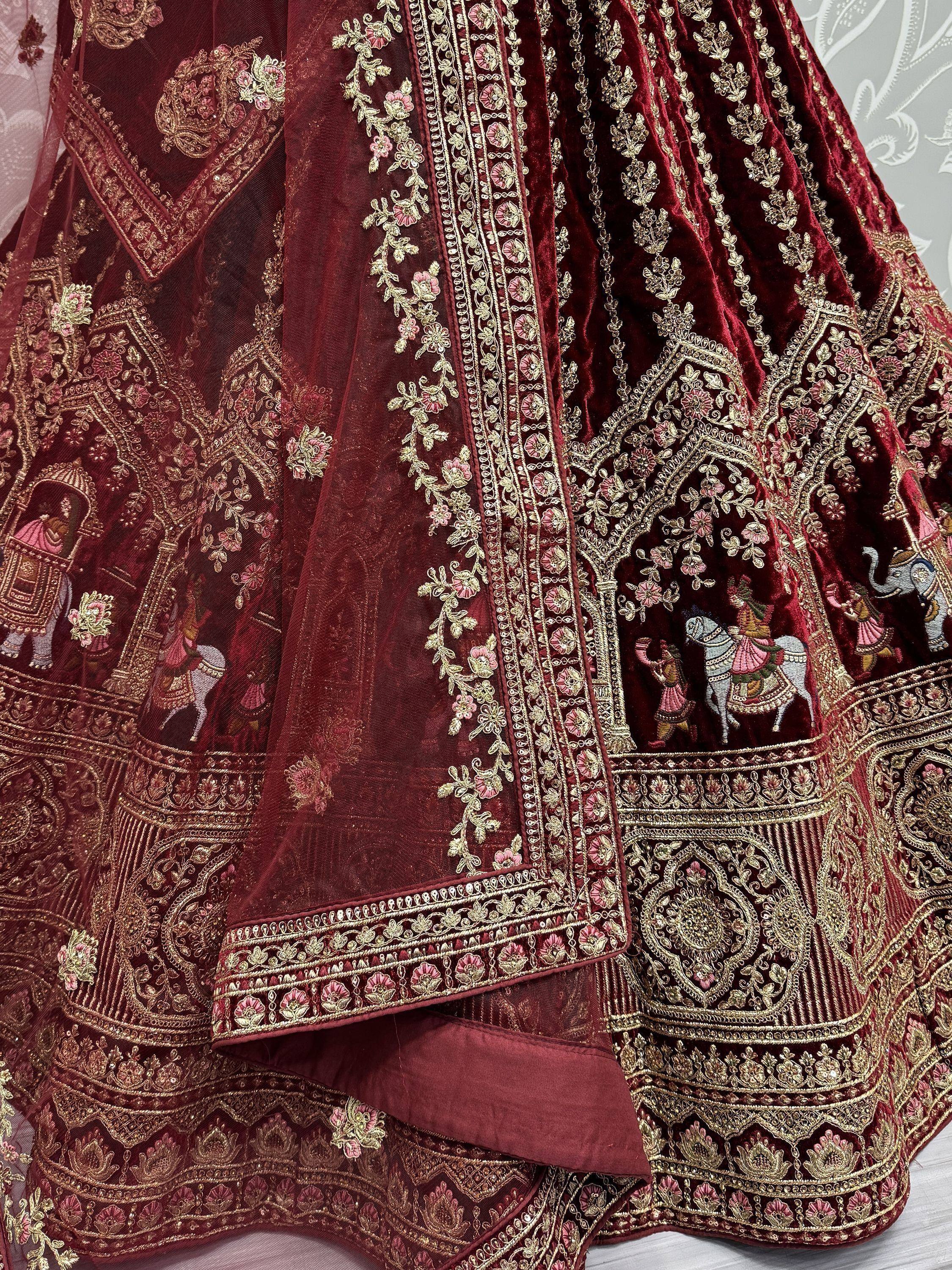 Luxury maroon velvet lehenga with gold embroidery, floral motifs, and royal scenes for Indian weddings