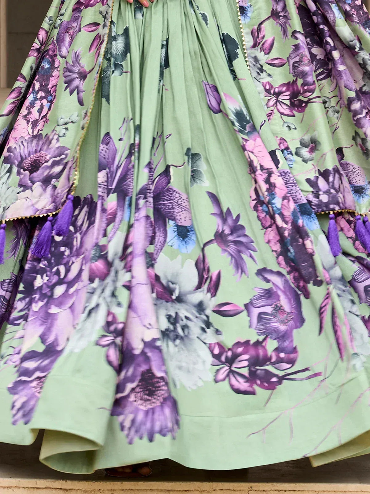 Green floral lehenga with purple and pink blooms, gold trim, and tassels for ethnic wear