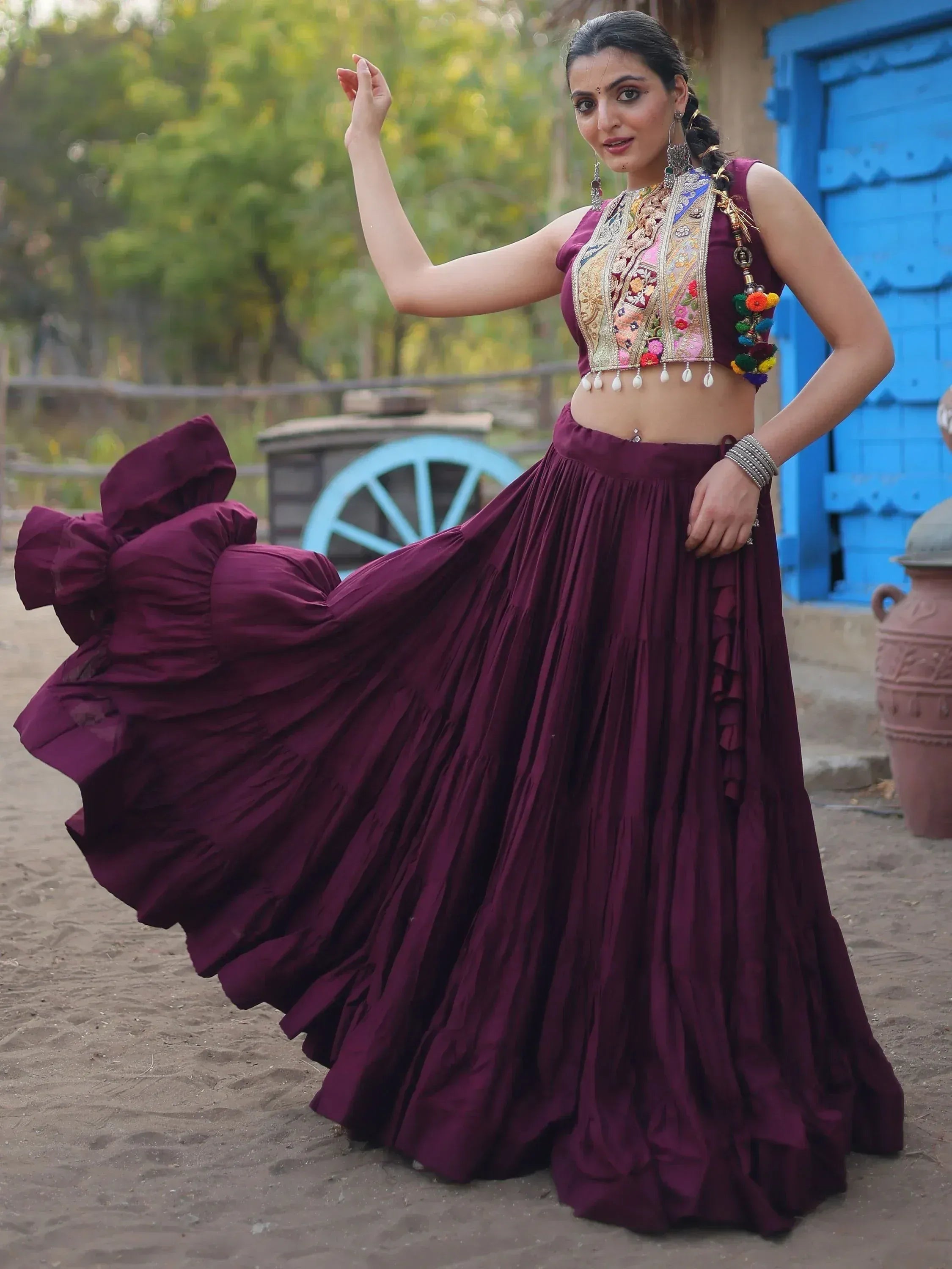Woman in maroon embroidered lehenga choli with floral blouse, twirling outdoors near blue door