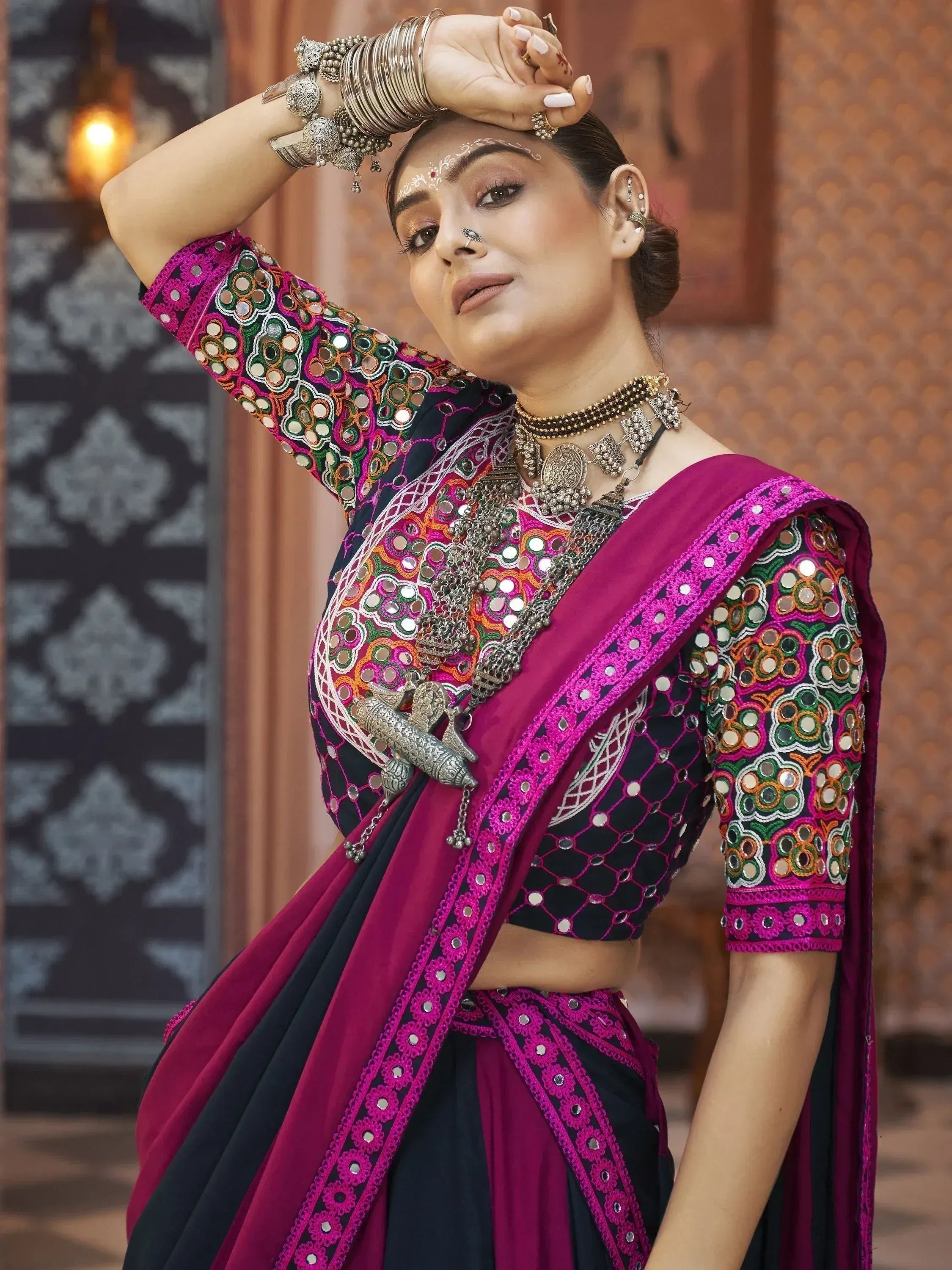 Woman in vibrant mirror-work ethnic saree with pink border, traditional jewelry, and nose ring