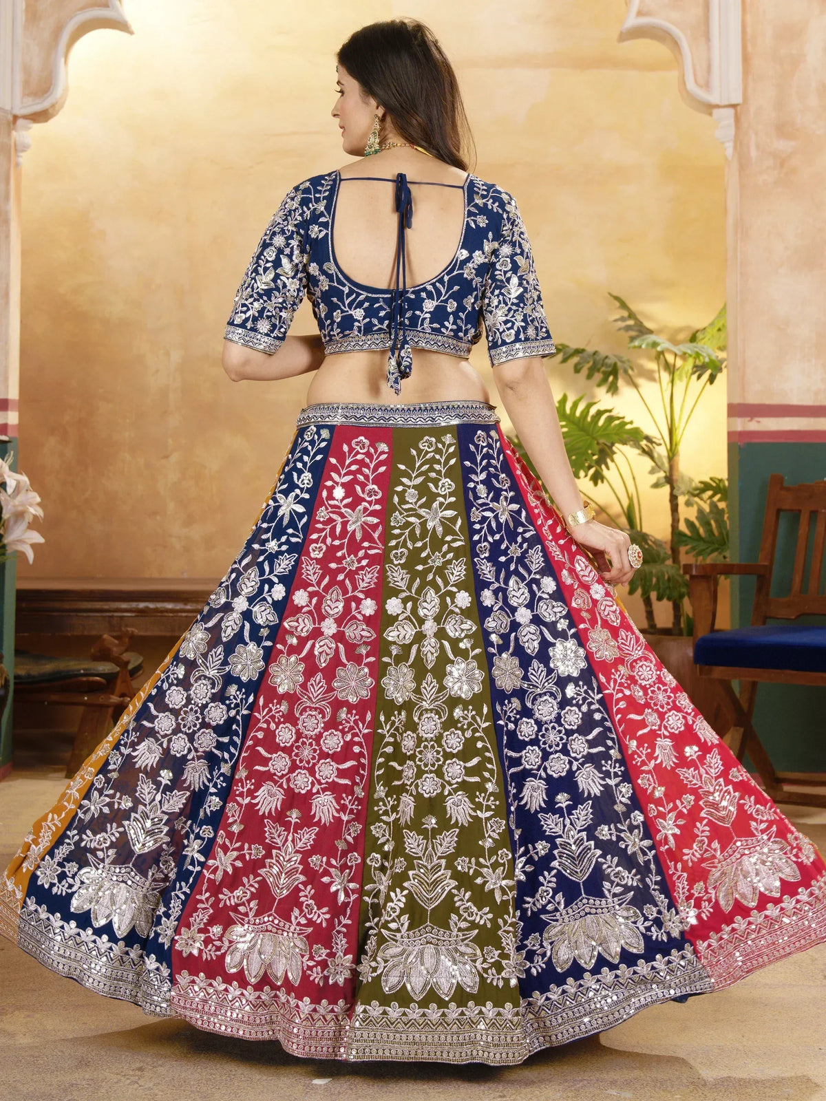 Woman in blue, red, and green embroidered lehenga choli with floral patterns, back view