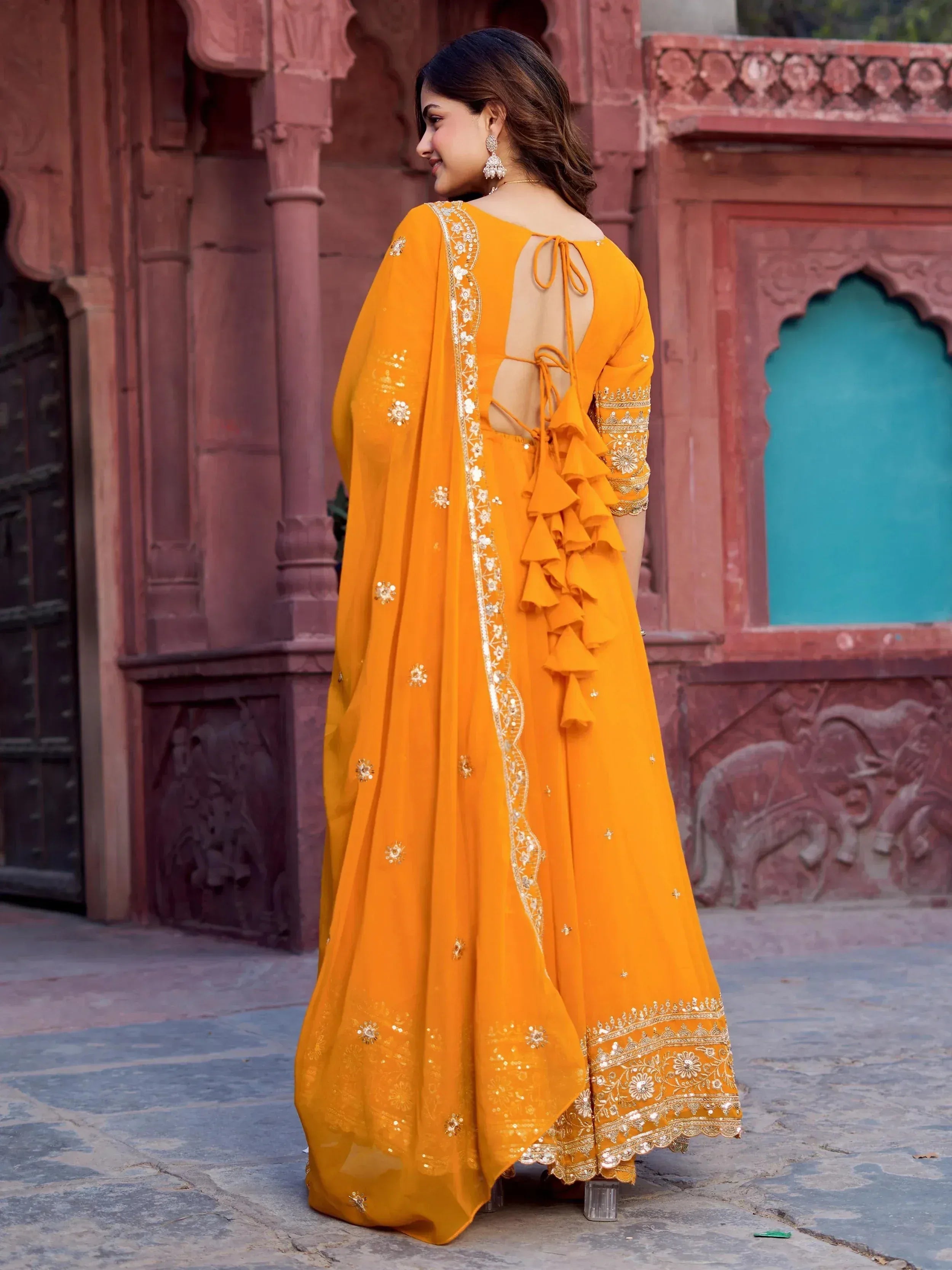 Vibrant orange ethnic gown with ruffles, embroidery, and back tie detail, perfect for Indian occasions