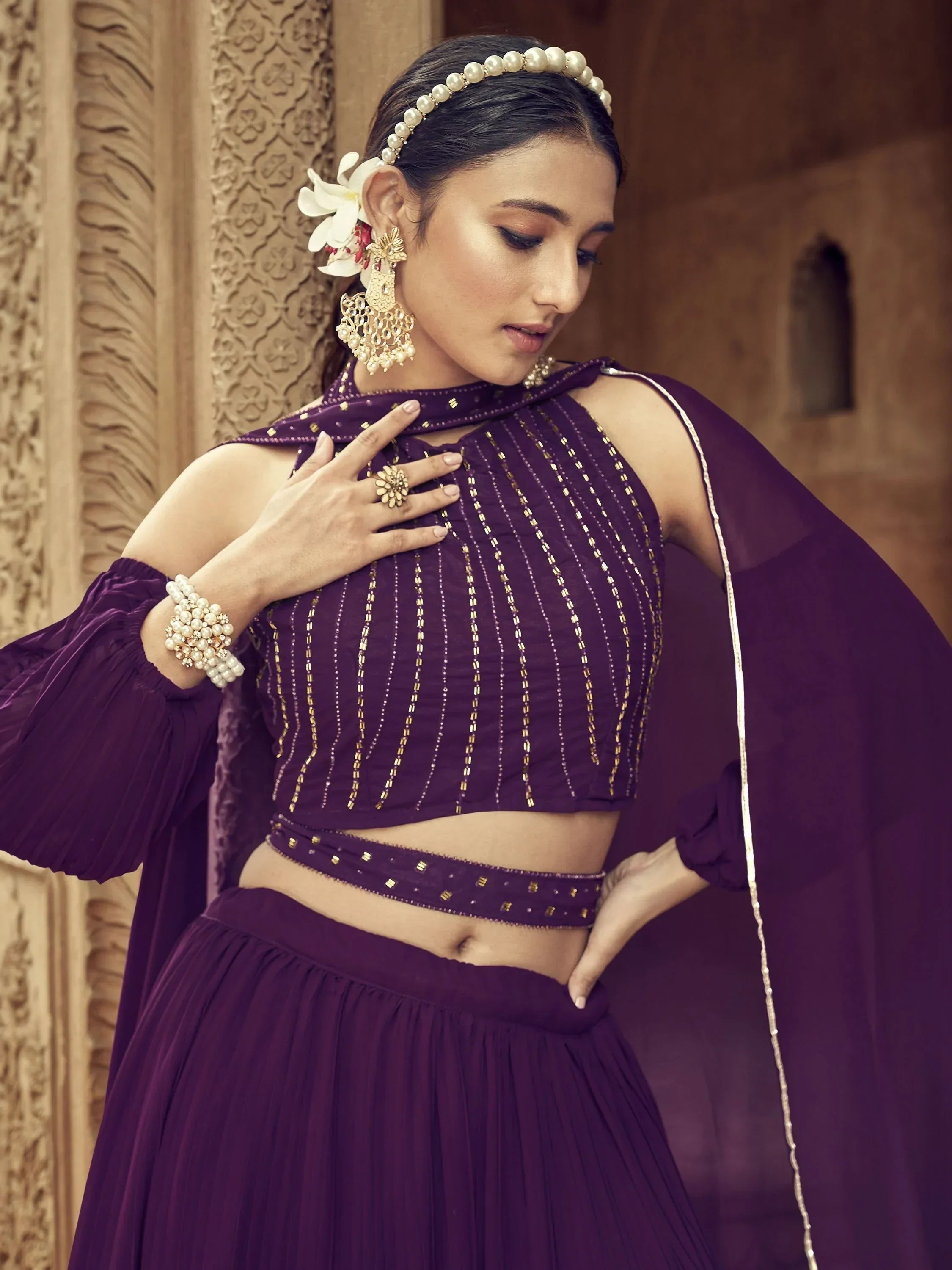 Purple ethnic lehenga choli with gold embroidery, pearl jewelry, and floral hair accessory