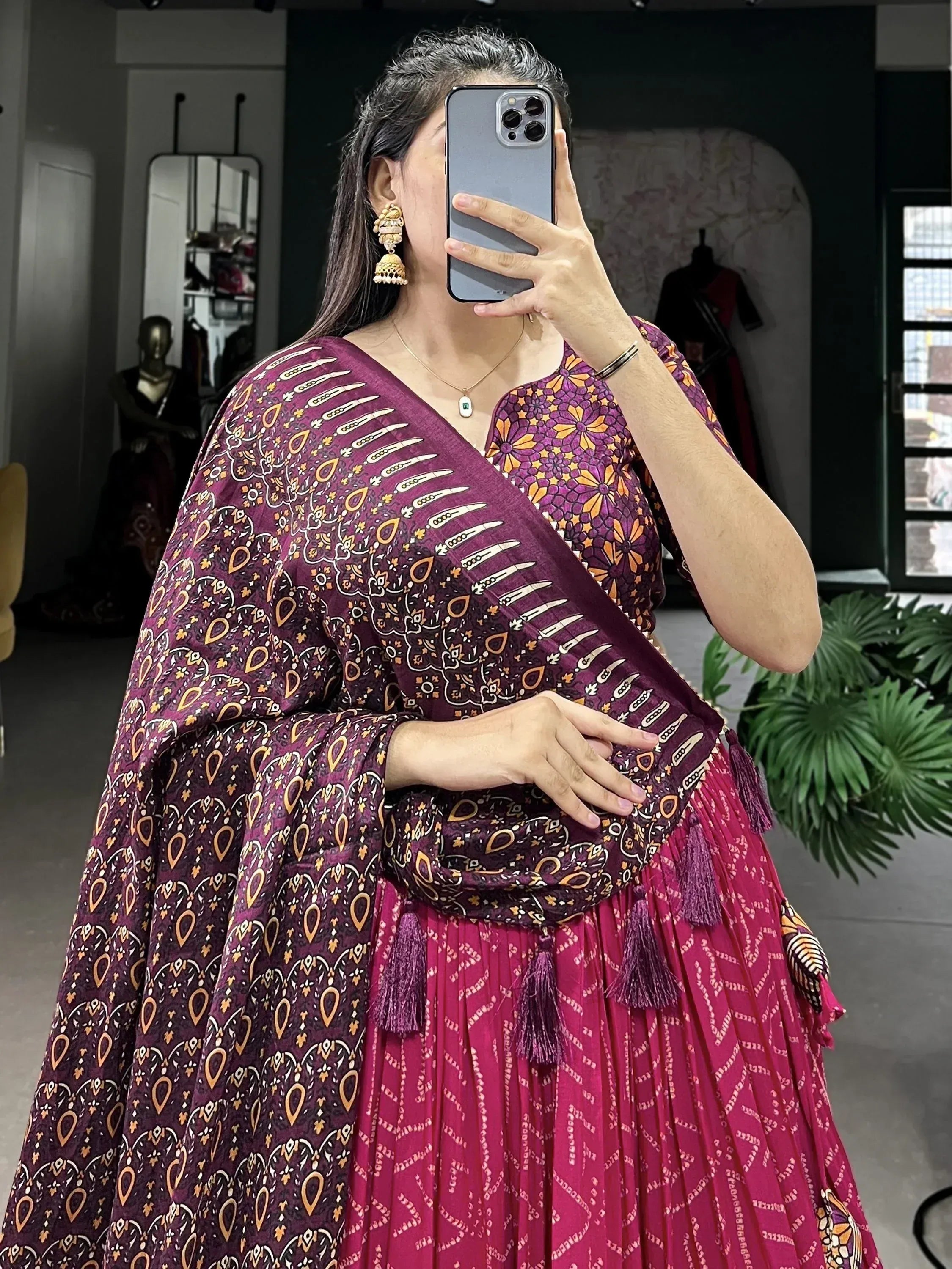 Woman in purple printed ethnic gown with tassels, taking mirror selfie in boutique