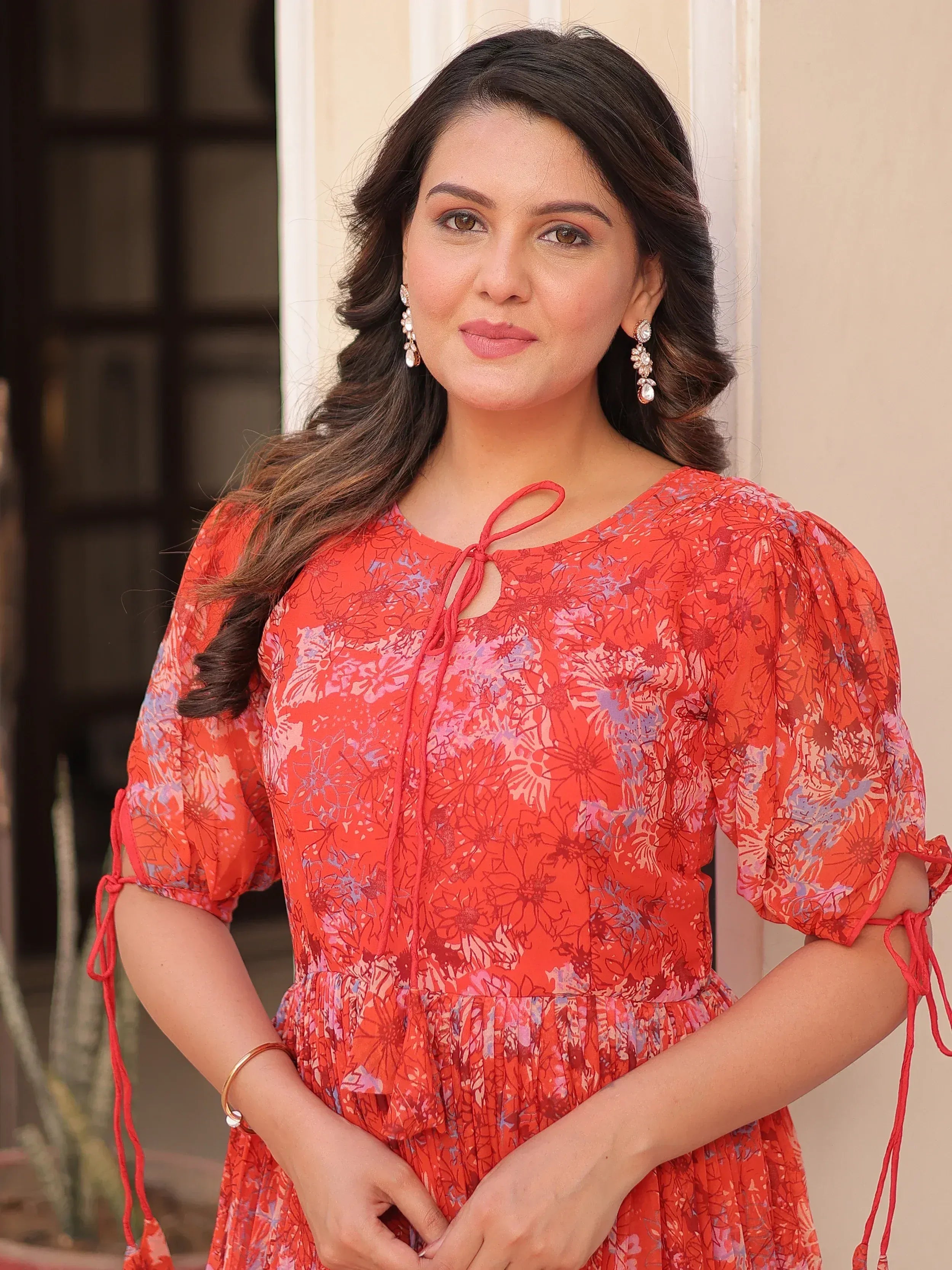 Woman in vibrant red floral ethnic gown with puff sleeves and tie-up details, perfect for festive occasions.
