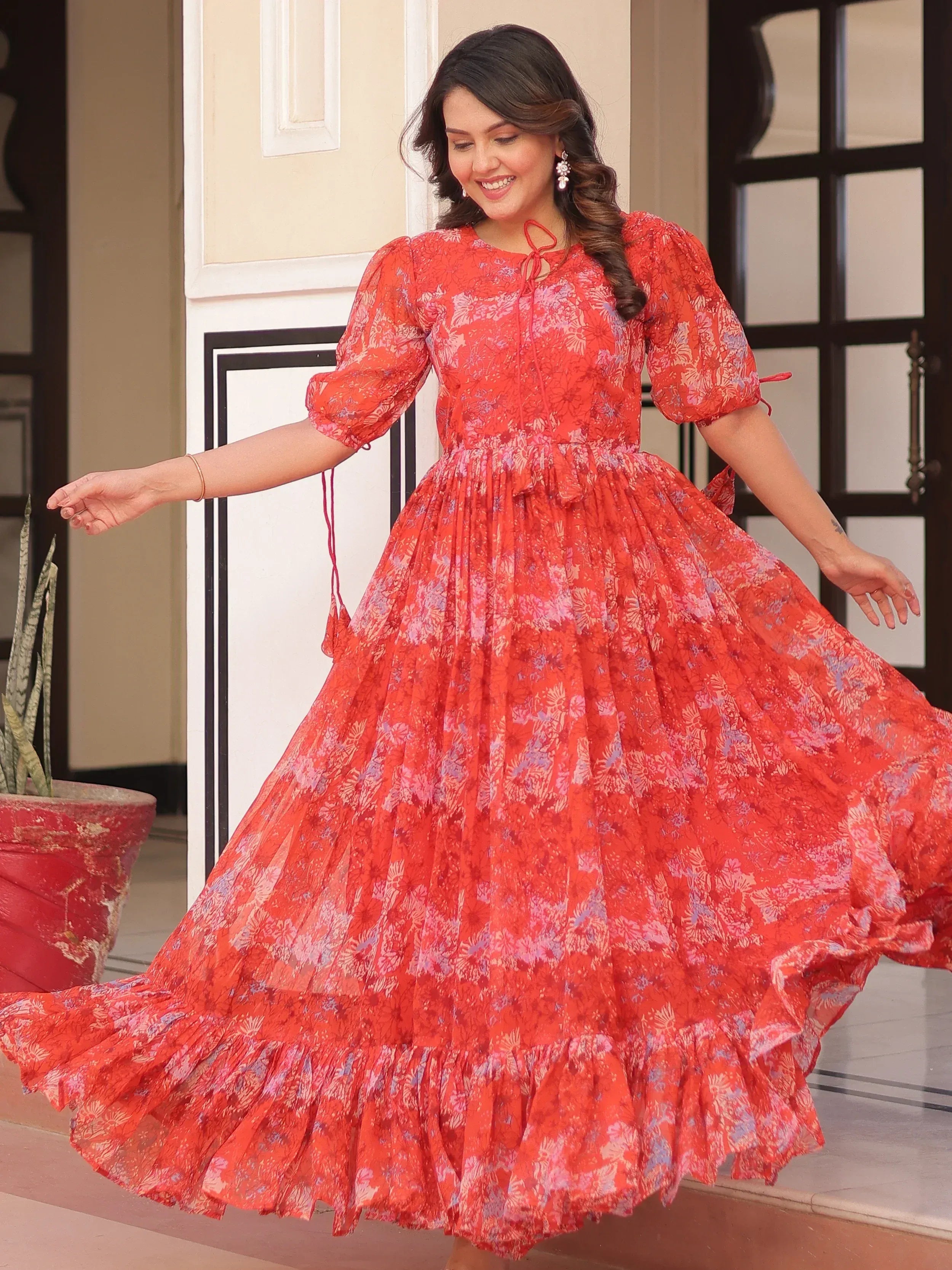 Woman twirling in vibrant red floral ethnic gown with puff sleeves and ruffled hem