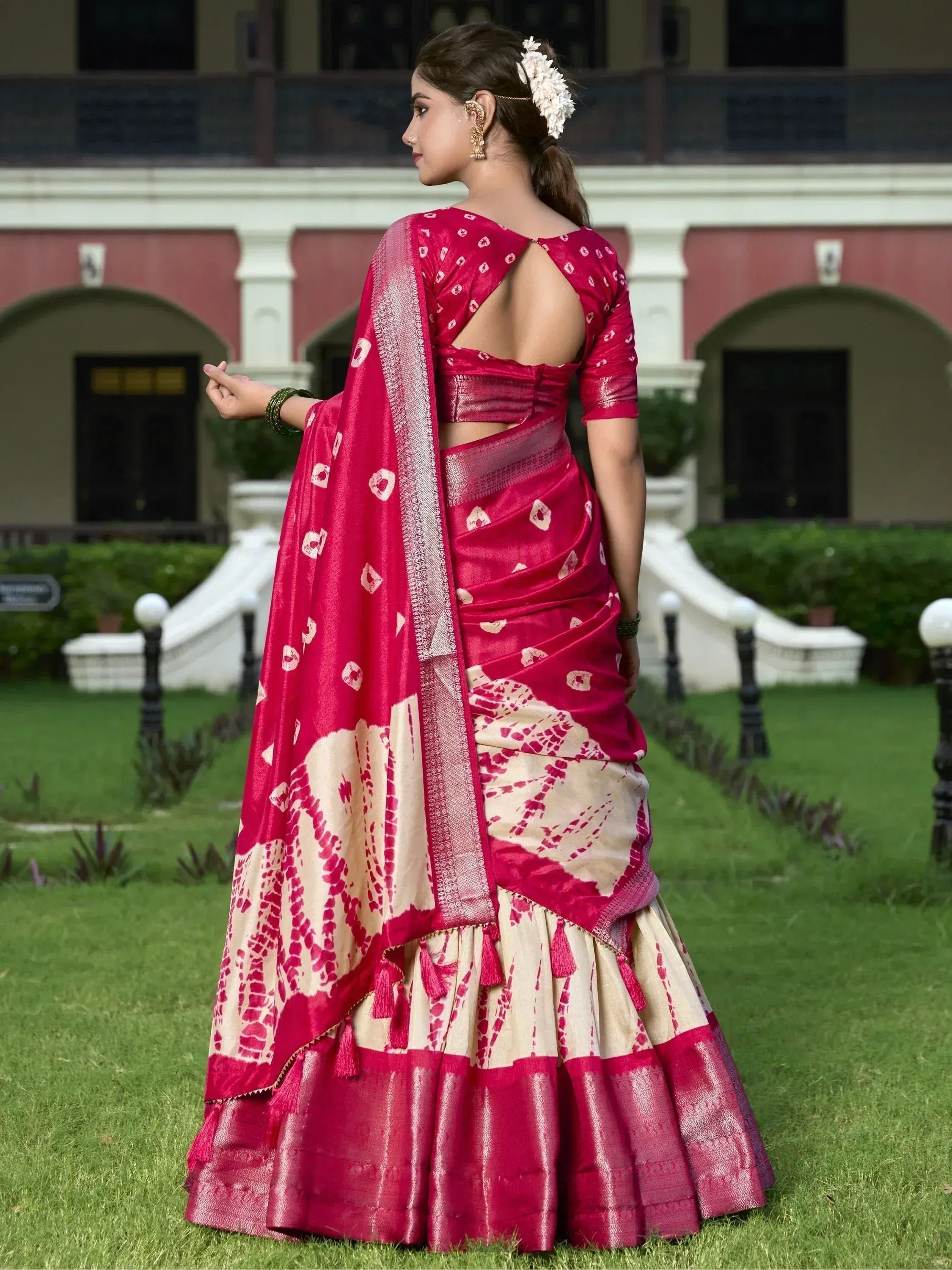 Woman in pink and cream printed saree with backless blouse, floral hair accessory, standing outdoors