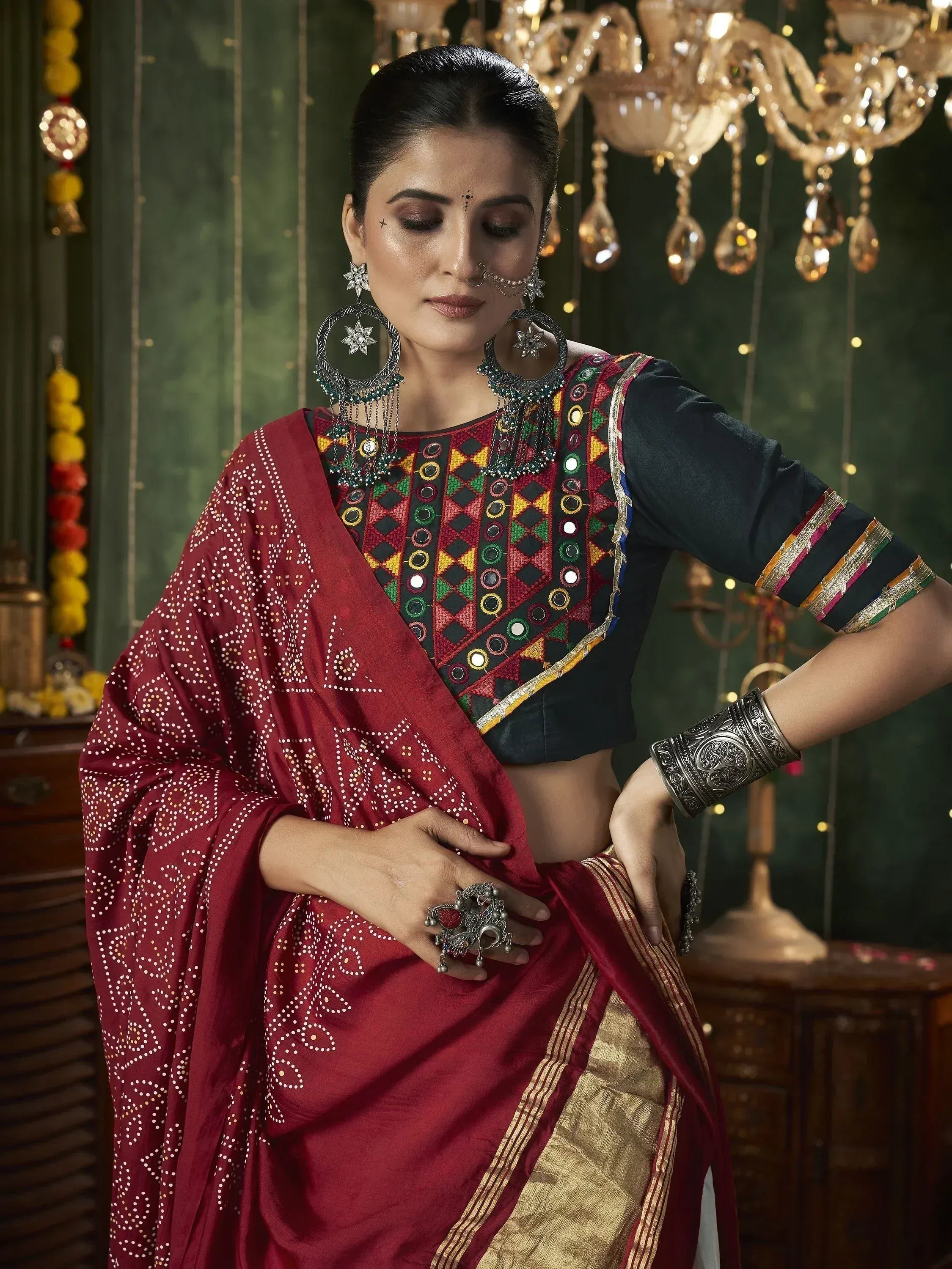 Woman in maroon ethnic saree with mirror work blouse, traditional jewelry, and festive decor