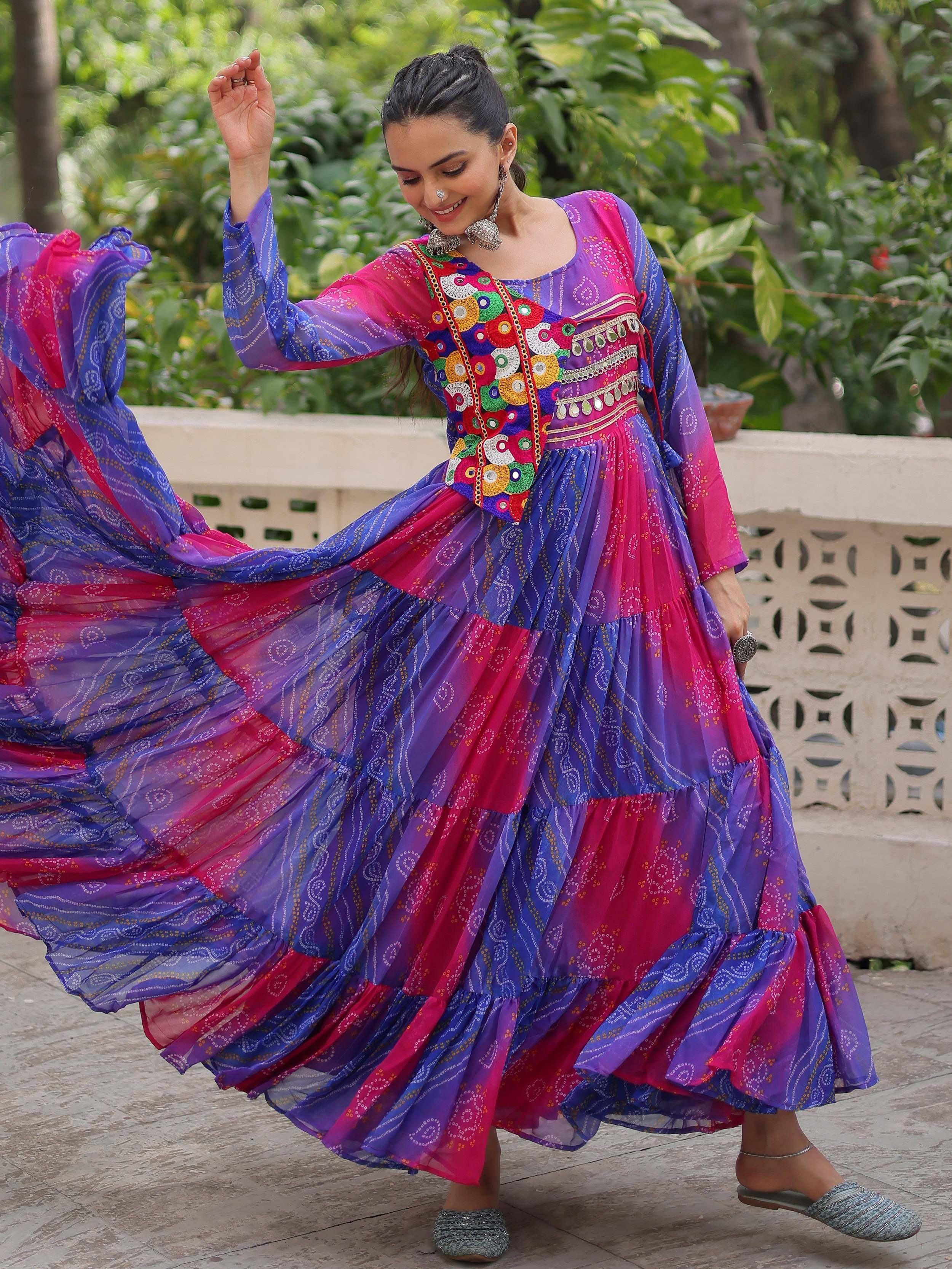 Woman twirling in vibrant purple and pink ethnic gown with mirror work, perfect for festive occasions.