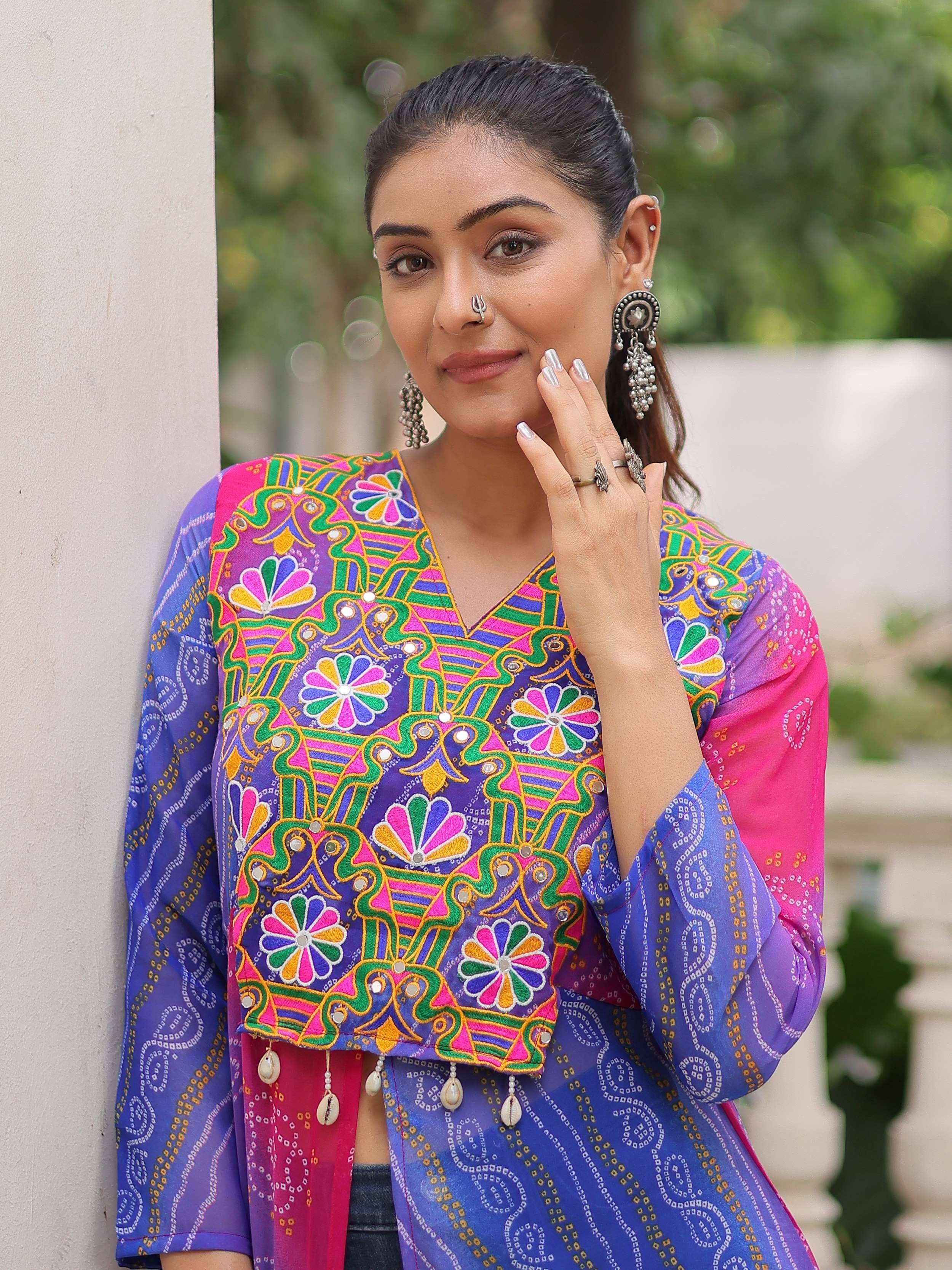 Woman in vibrant Indian ethnic top with colorful embroidery, mirror work, and floral patterns, paired with statement earrings.