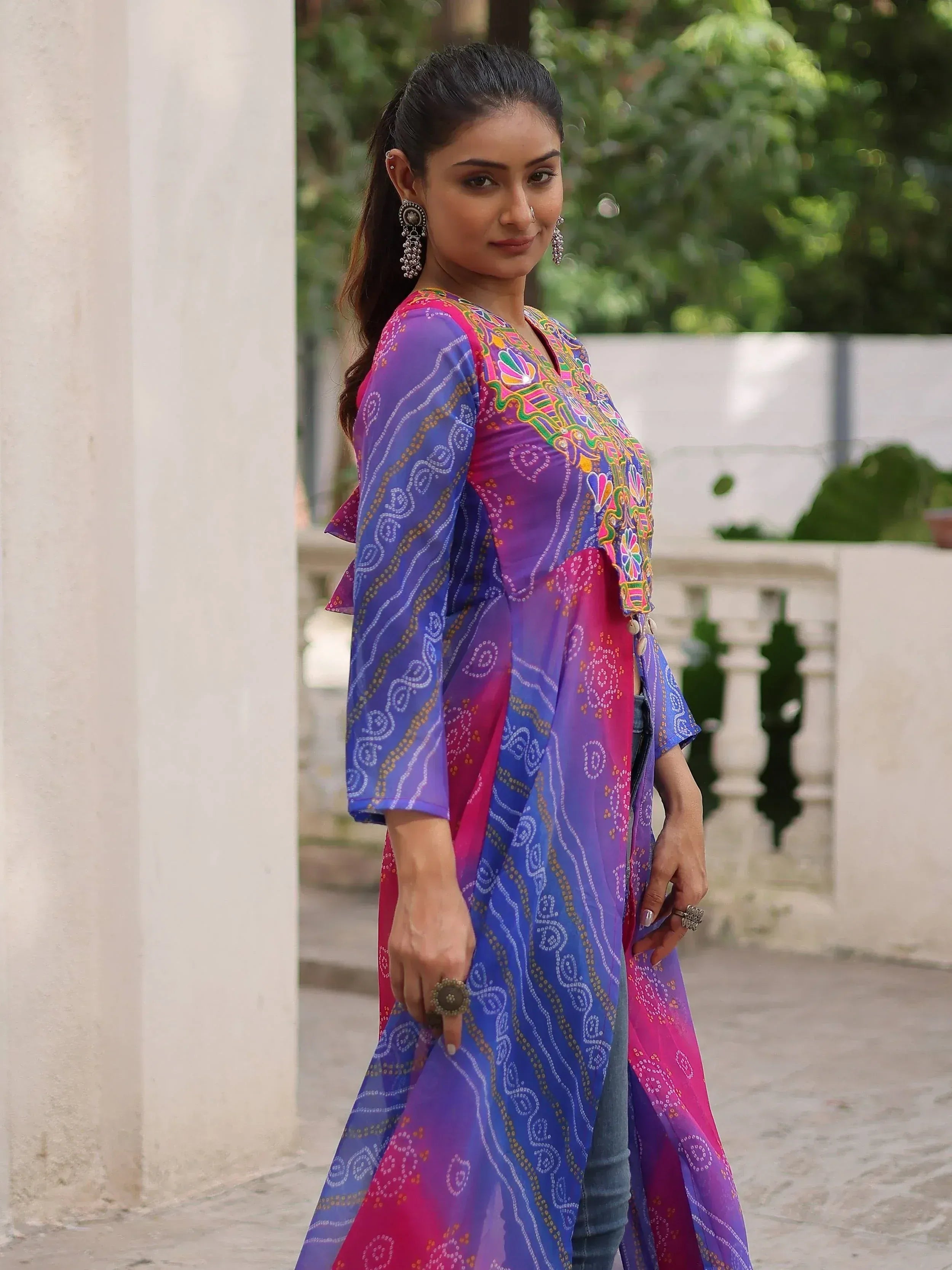 Woman in colorful embroidered Indian ethnic kurta with blue and pink patterns, styled with jeans and jhumka earrings
