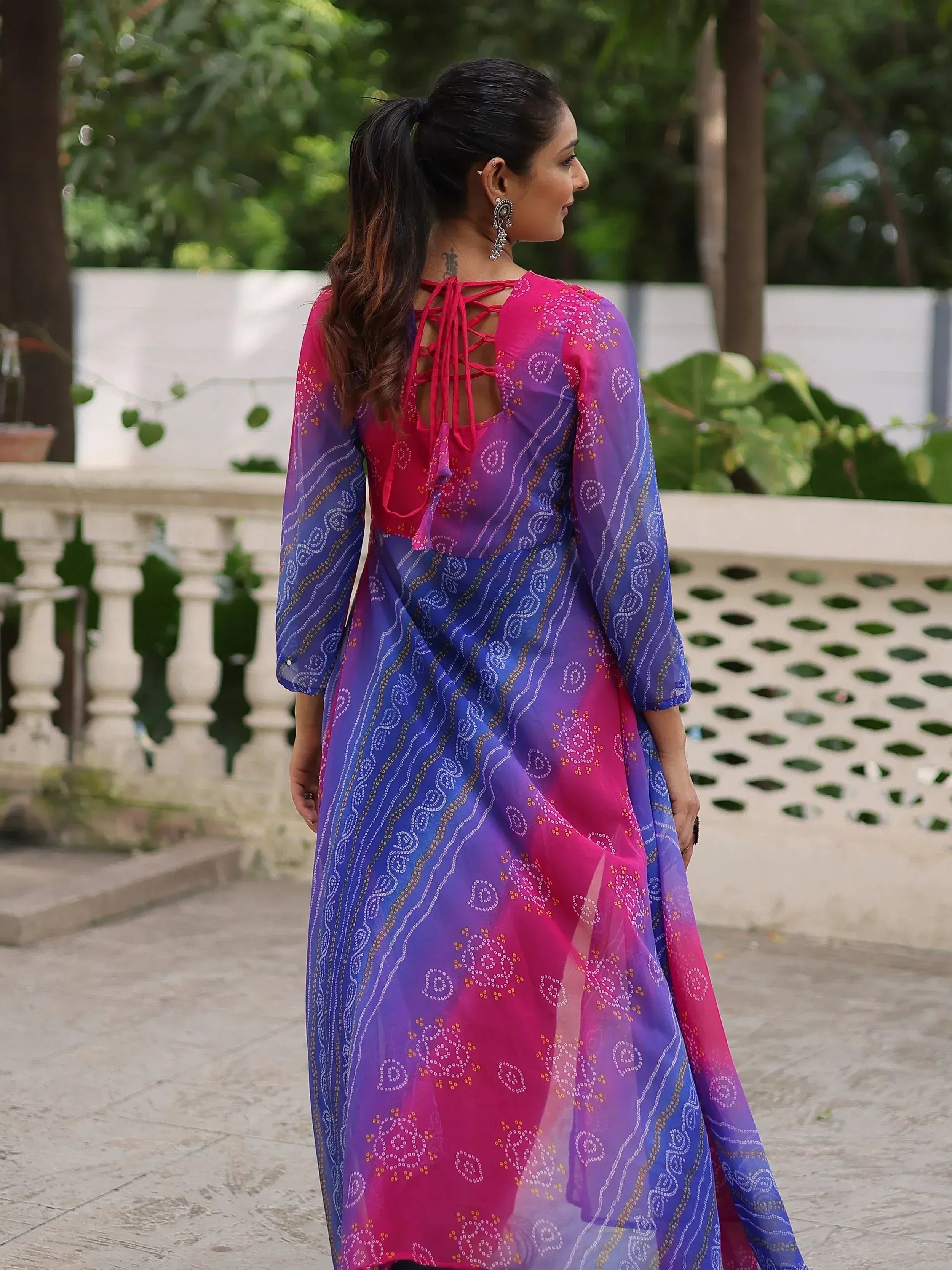 Woman in vibrant pink and blue printed ethnic gown with lace-up back, perfect for Indian occasions.