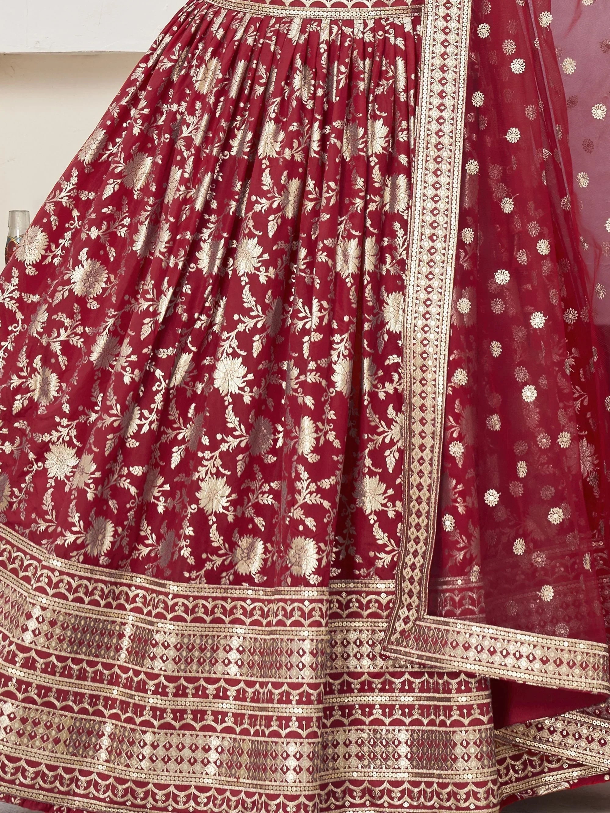 Red and gold floral embroidered lehenga choli with intricate border detailing, perfect for Indian ethnic wear.