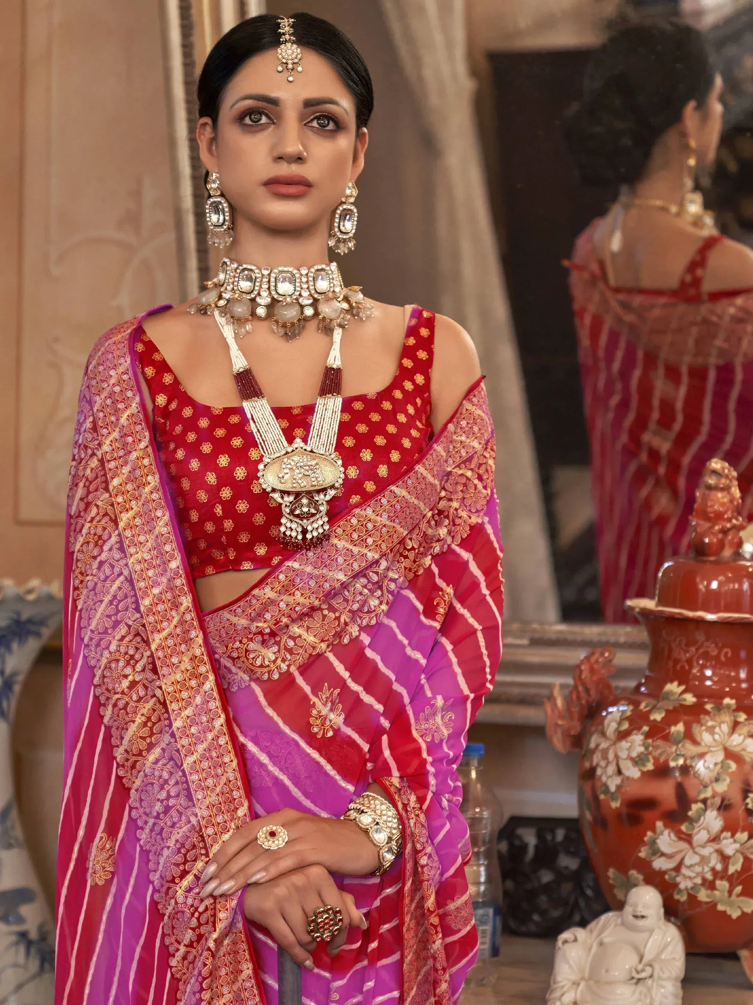 Woman in red and pink ethnic saree with gold embroidery, traditional jewelry, and statement necklace for festive occasions