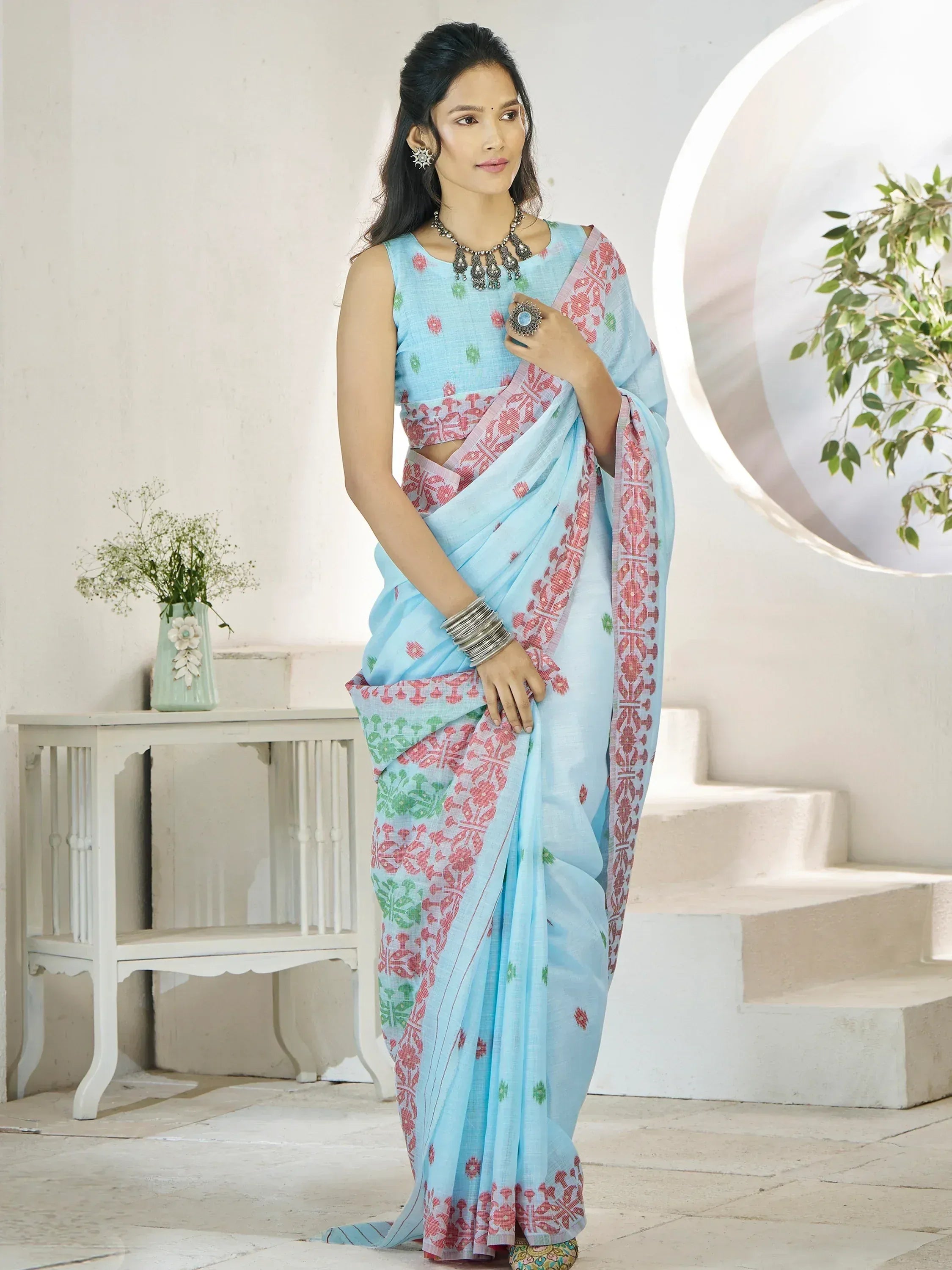 Light blue printed saree with pink and green floral motifs, paired with matching sleeveless blouse, styled for ethnic occasions.