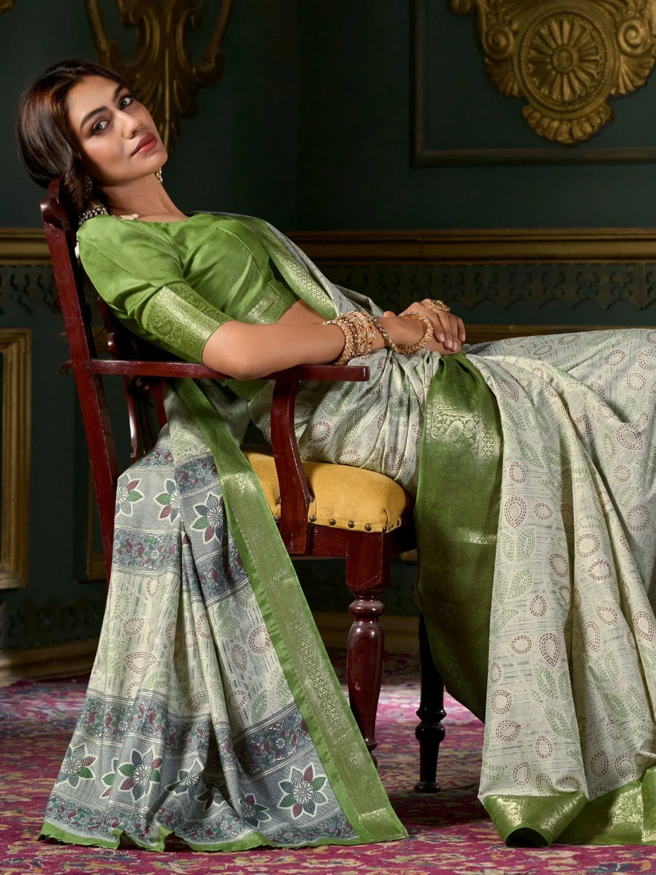 Woman in elegant green and silver printed saree with floral border, styled with gold jewelry for ethnic occasions.
